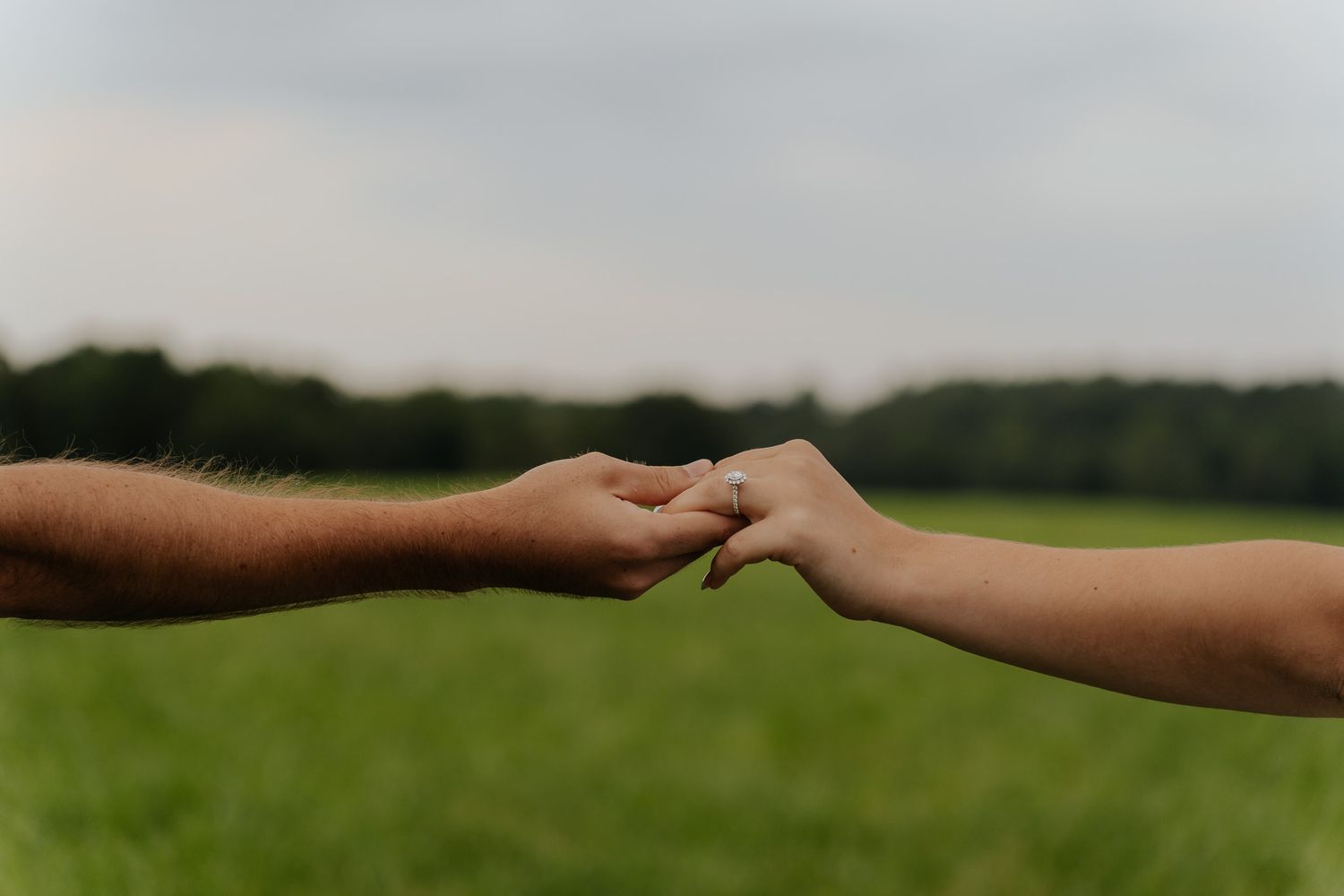 Two people reaching toward each other holding hands in a green field under an overcast sky.