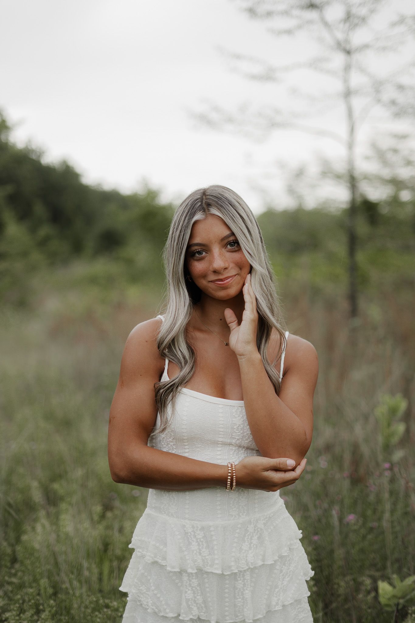 Young woman in white tiered ruffle dress posing confidently in a natural green field setting.