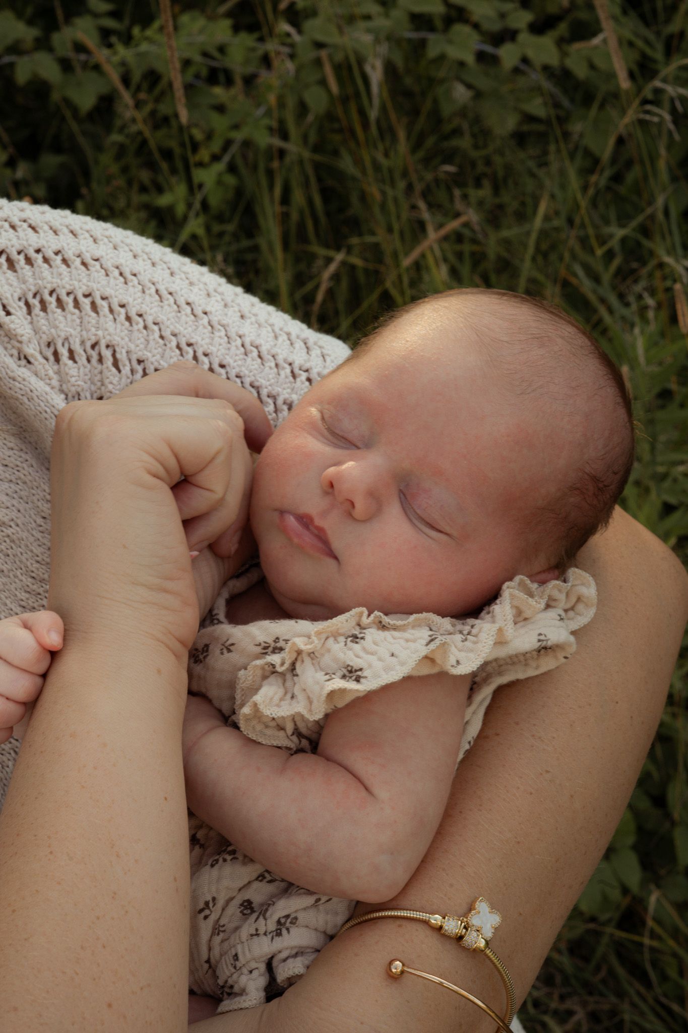 Peaceful newborn baby sleeping in mothers arms wrapped in a soft white knit blanket outside.