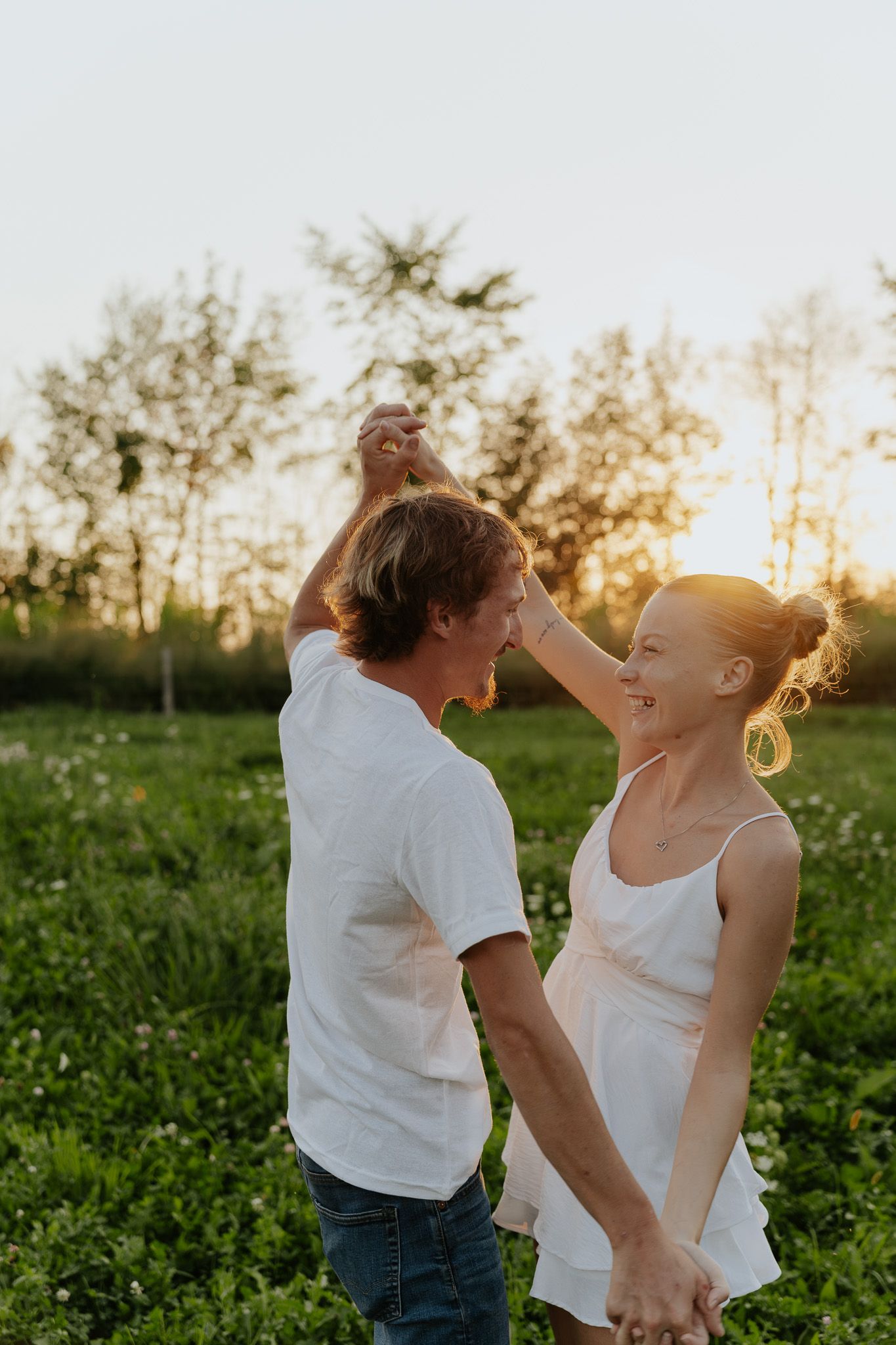 Couple dancing and spinning together in a sunlit green meadow during a warm golden sunset.