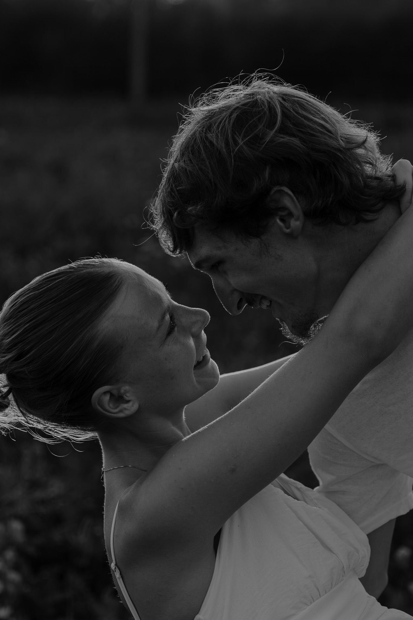 A couple laughs and embraces closely in an intimate black and white outdoor portrait.