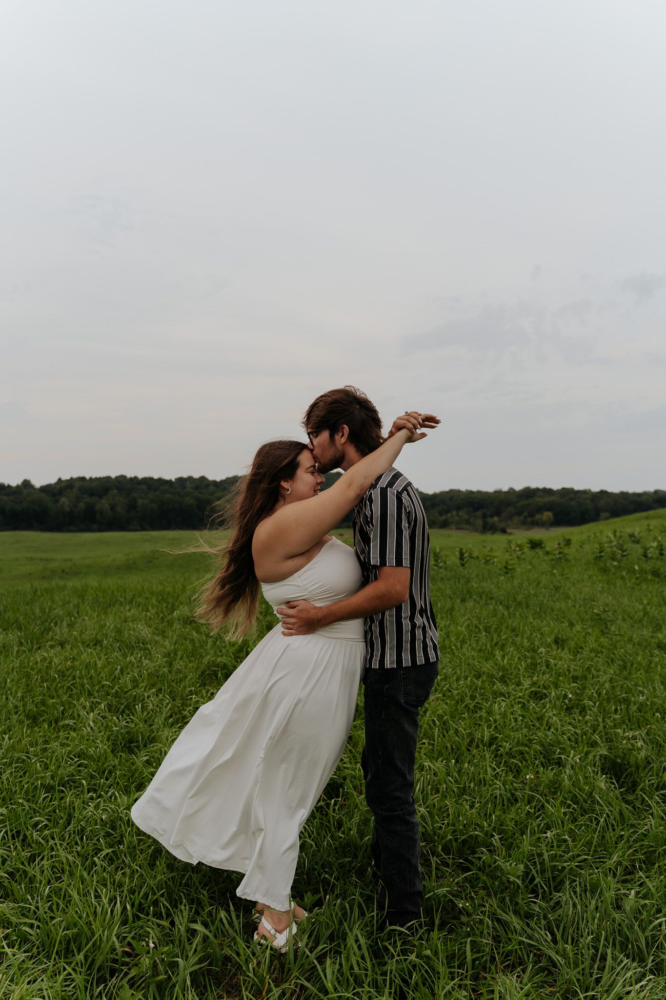 Romantic couple dancing and spinning together in a lush green open field under a cloudy sky.