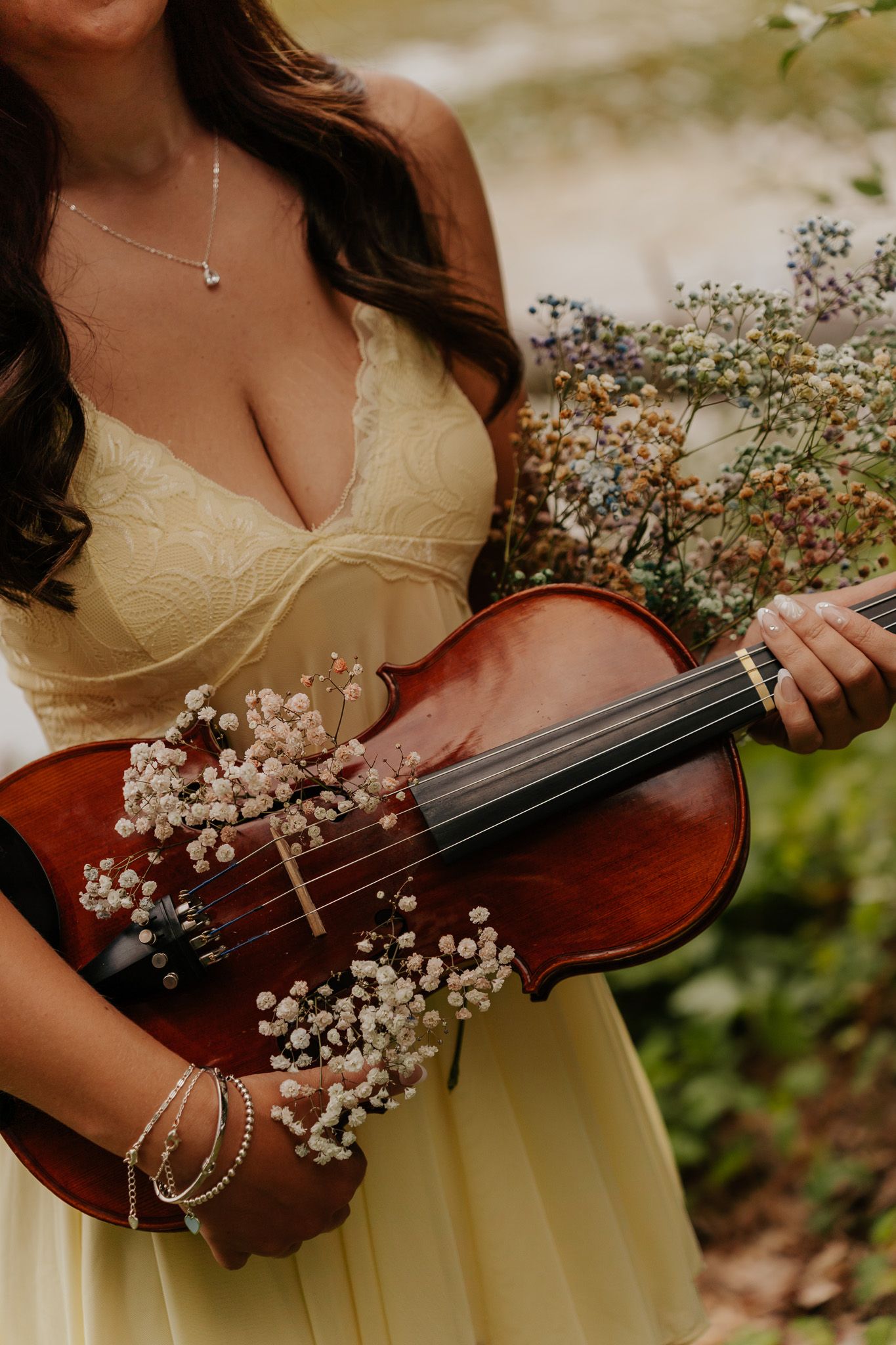 Woman in yellow dress holding violin decorated with baby's breath flowers.