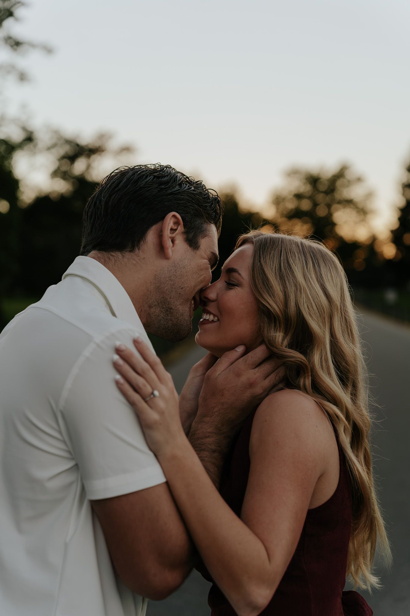 A couple shares a romantic moment at sunset, the woman smiling as the man leans in for a kiss outdoors.