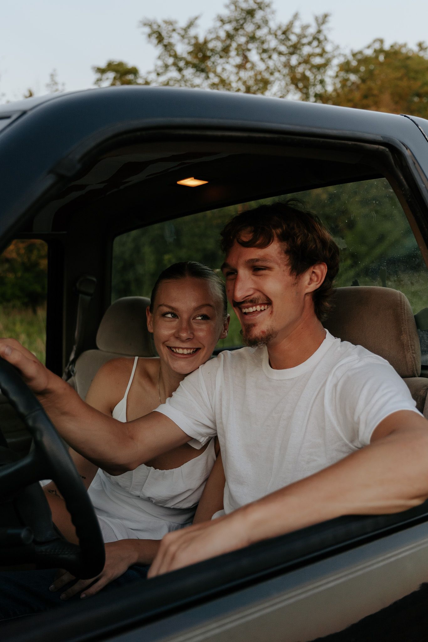A joyful couple sits in a vintage truck cab, the woman leaning on the man as he drives.