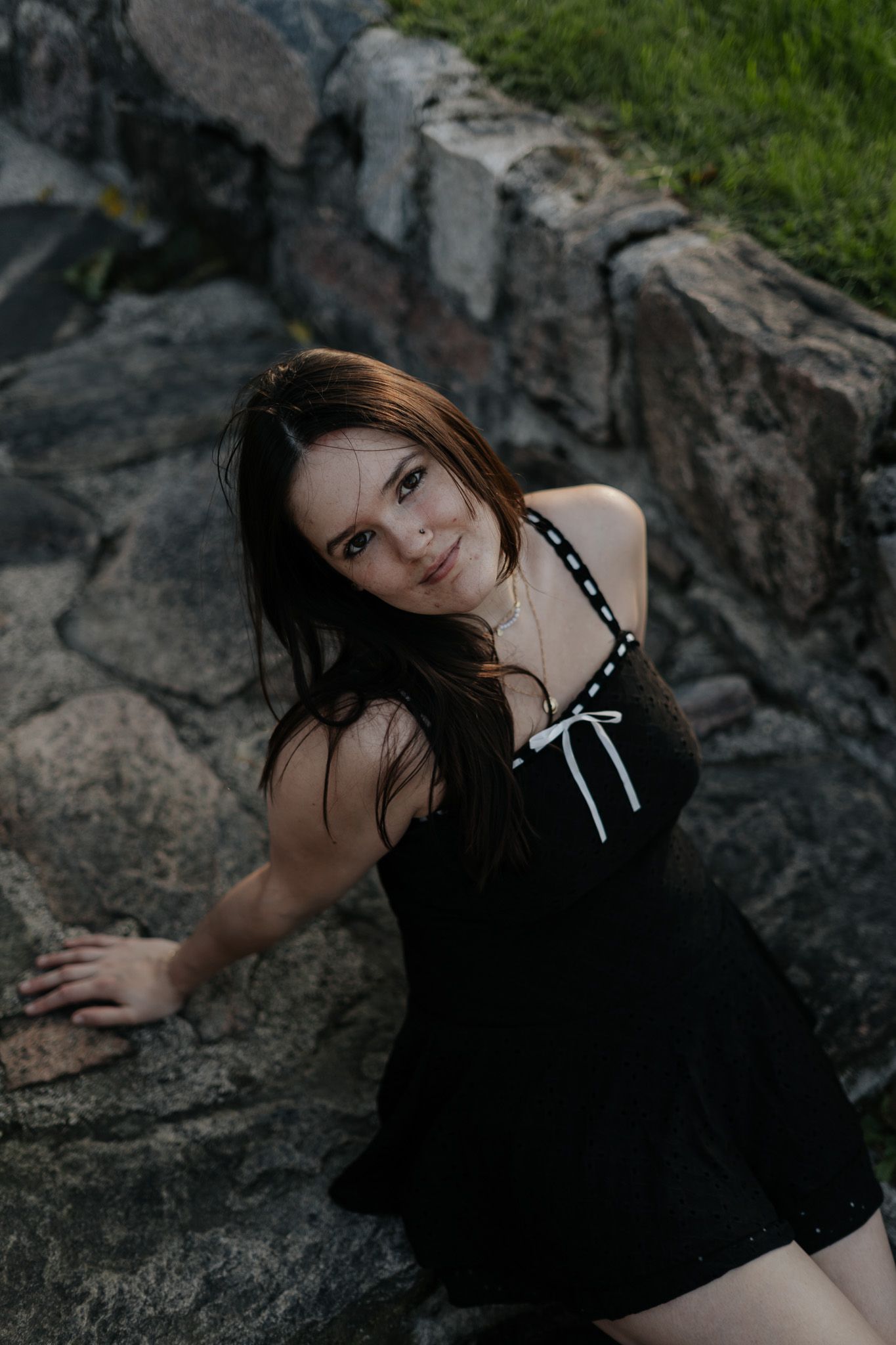 Young woman in black dress posing on rocky surface outdoors.