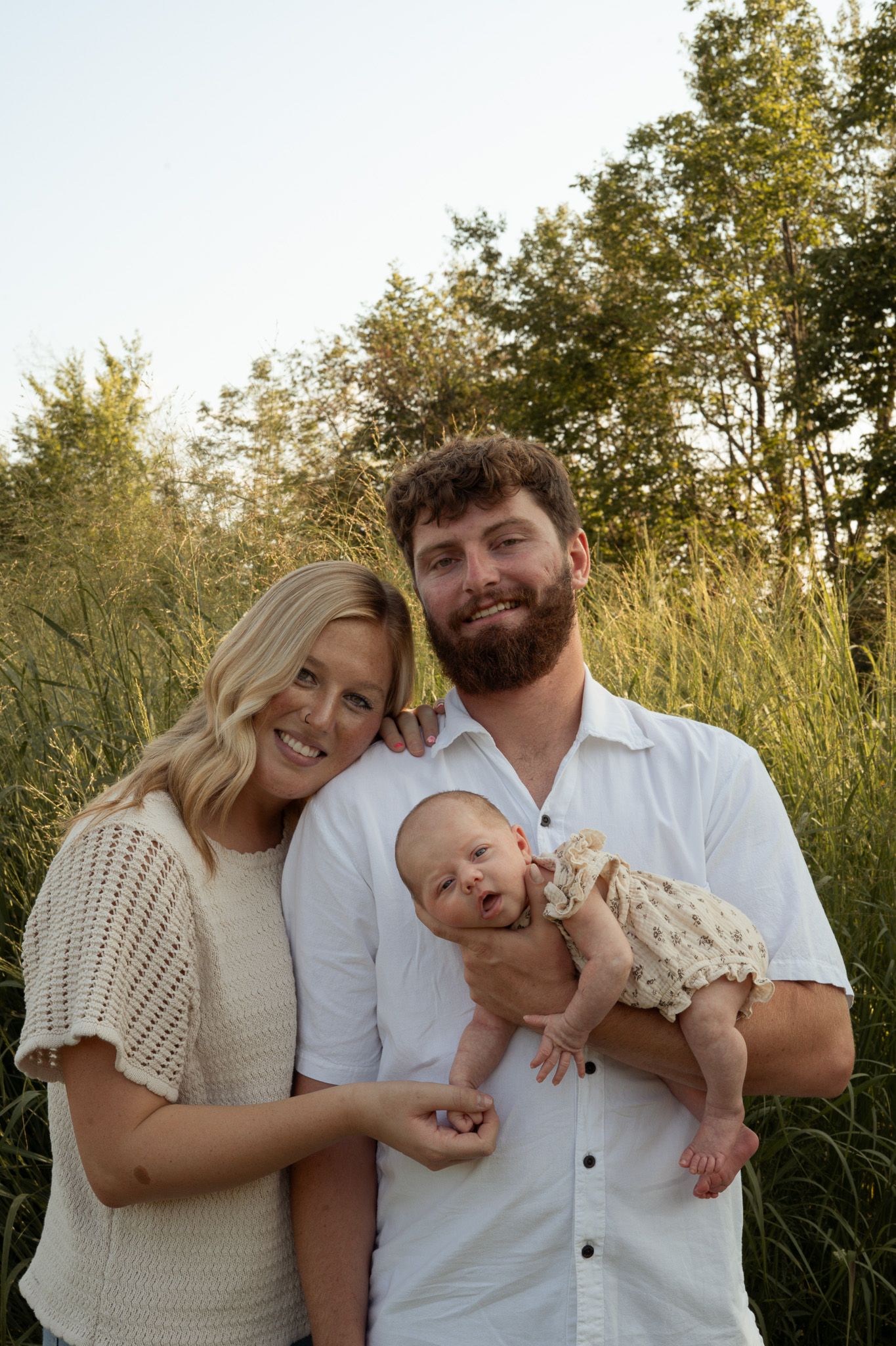 Happy young family with a bearded father and blonde mother holding their newborn baby outdoors.