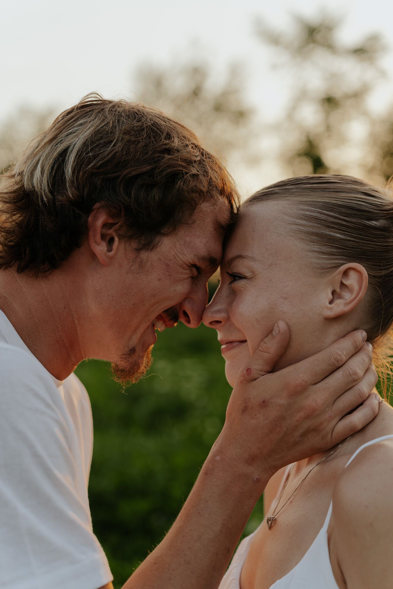 Romantic couple touching foreheads tenderly outdoors, man cradling womans face at sunset.