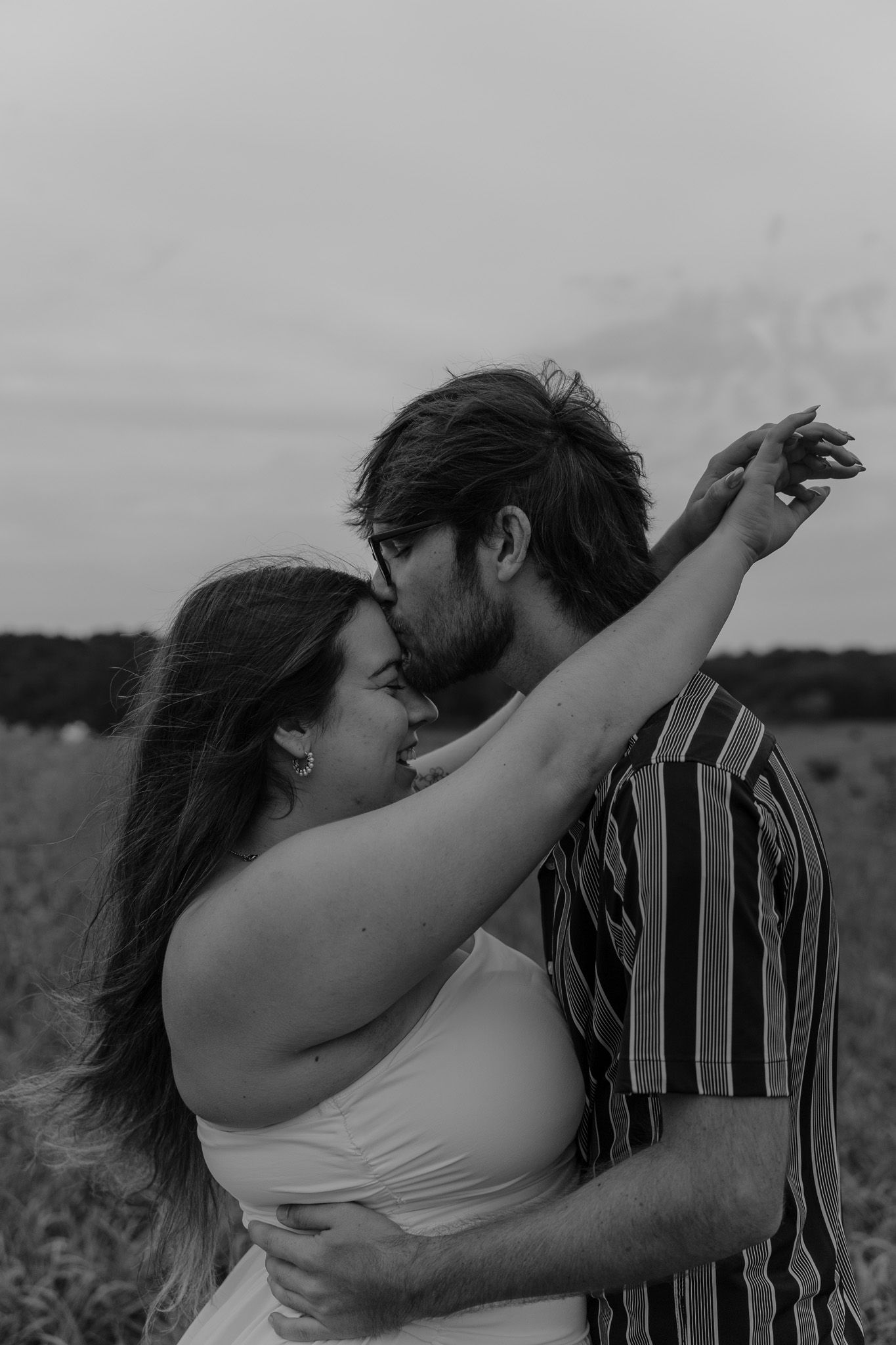 Black and white romantic photo of a couple about to kiss, embracing in an outdoor field setting.