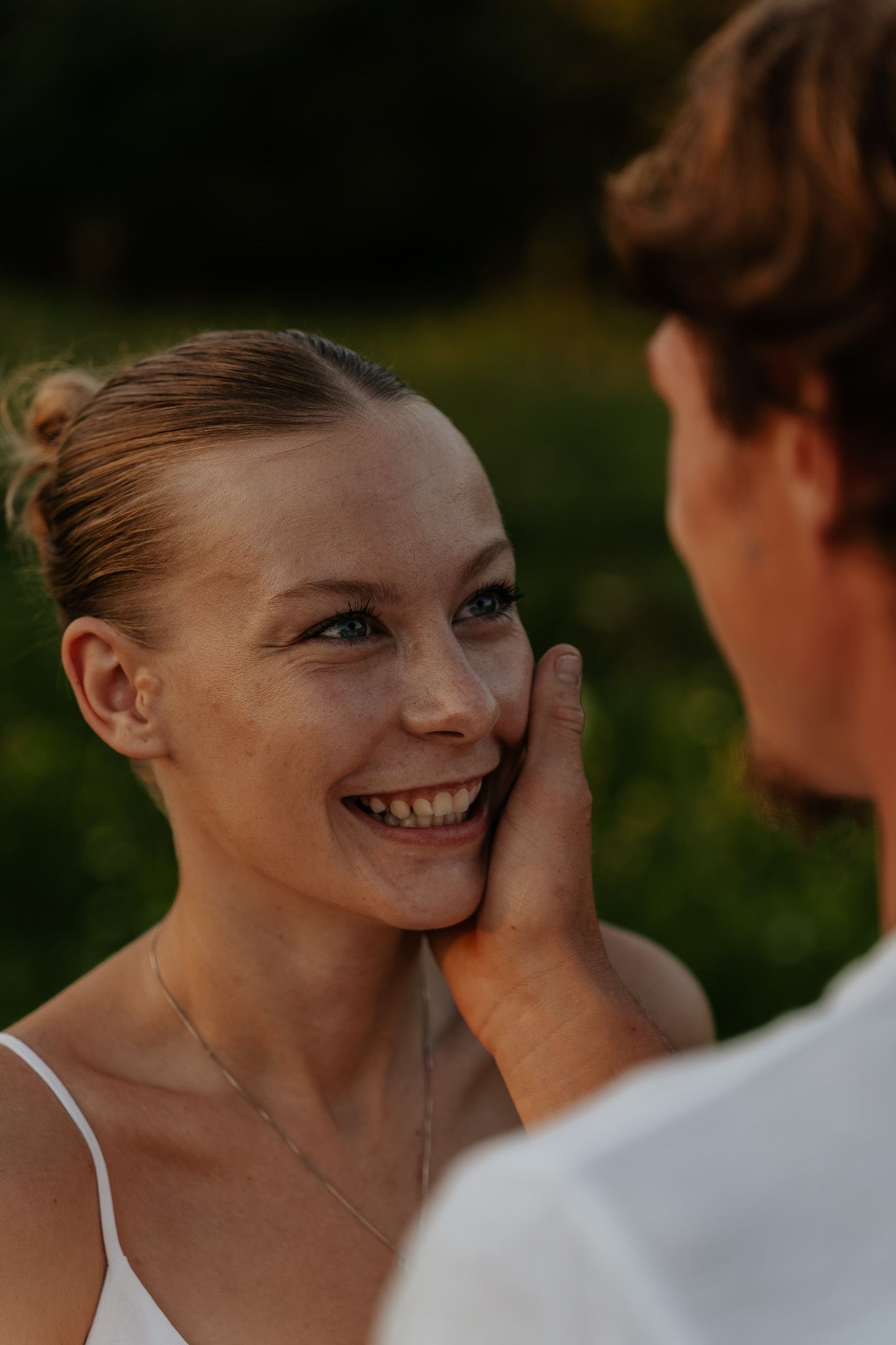 Happy woman smiling as man gently touches her face during romantic outdoor golden hour moment.