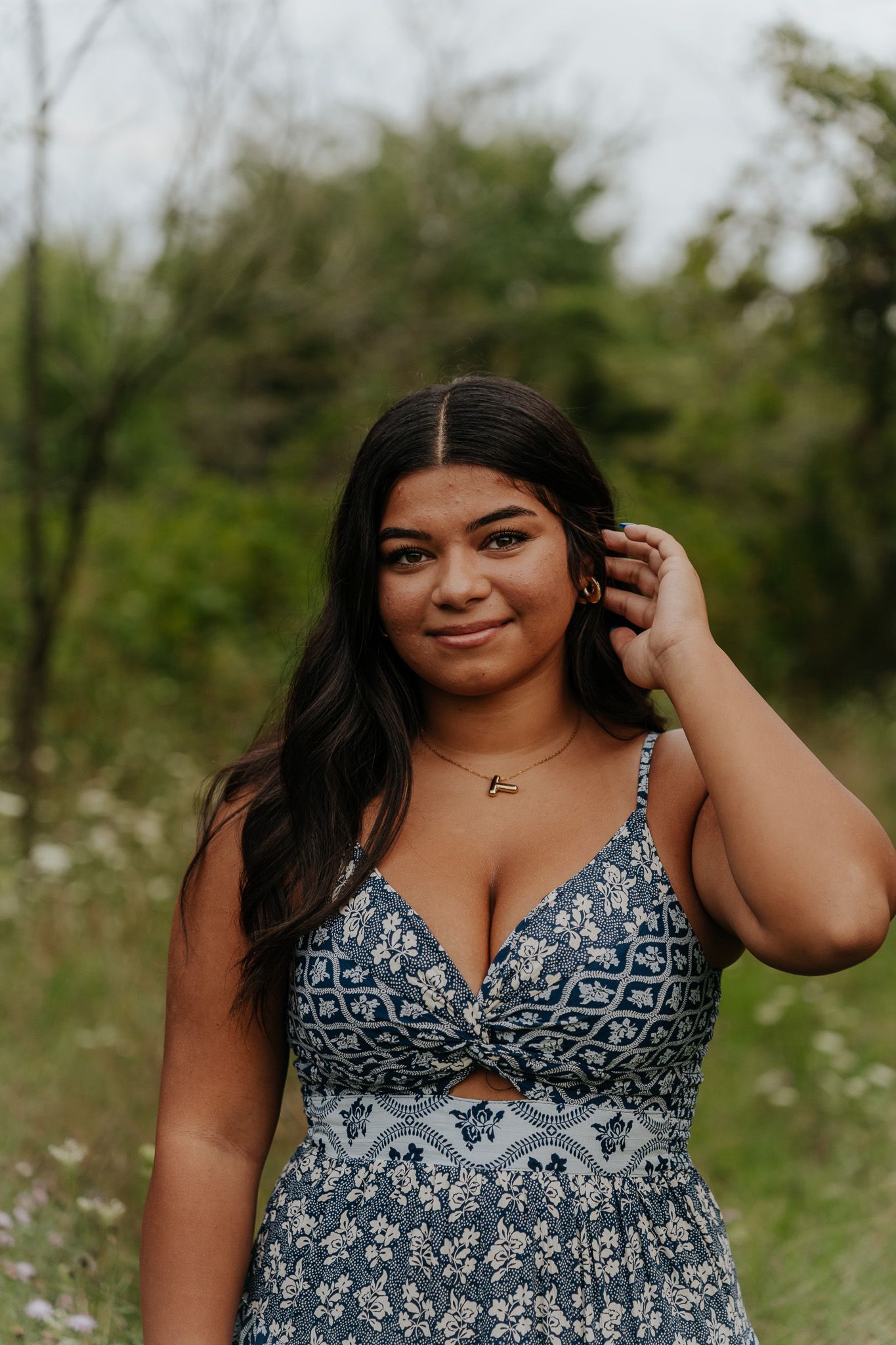 Young woman in blue floral maxi dress standing in wildflower field for outdoor senior portraits.