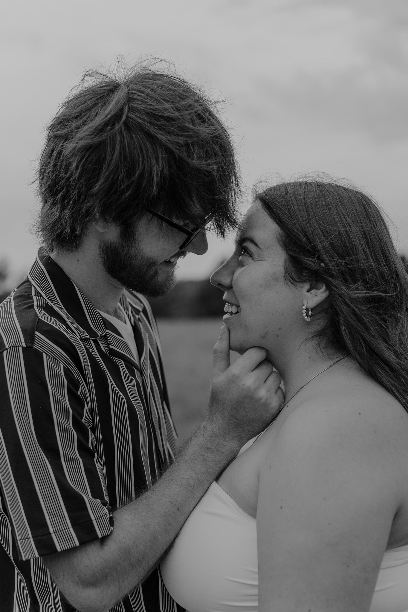 Black and white photo of a couple sharing a tender moment, man gently touching womans chin in a field.