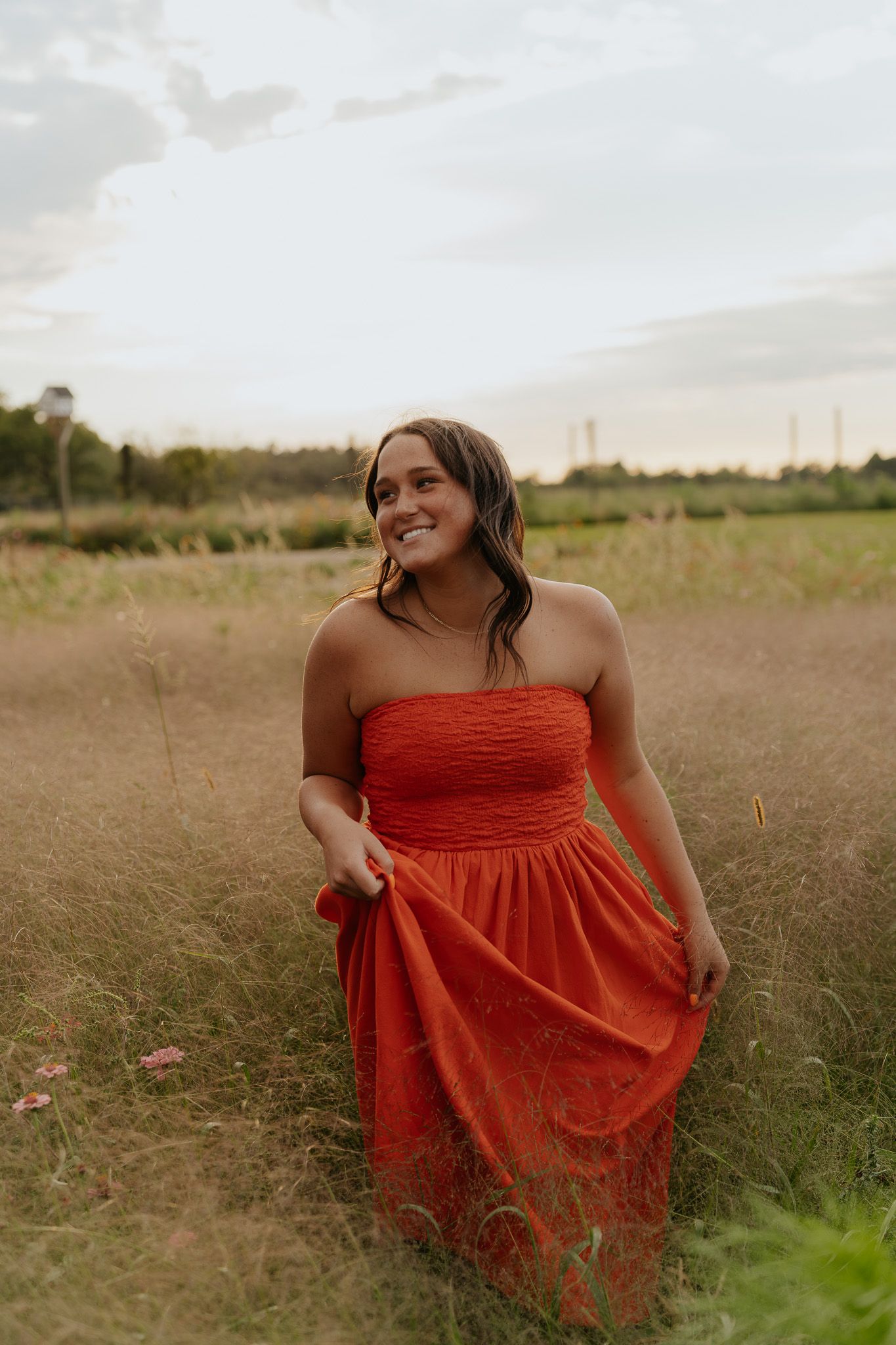 Young woman in red strapless dress smiling while walking through a wildflower field.
