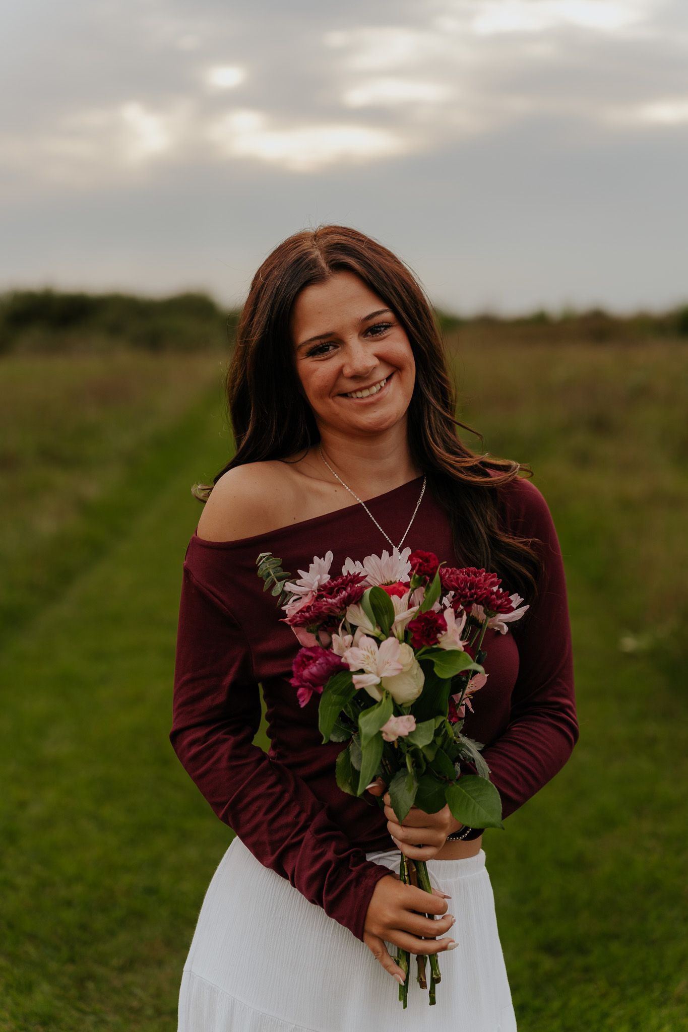 Smiling woman in burgundy top holding colorful flower bouquet in field.