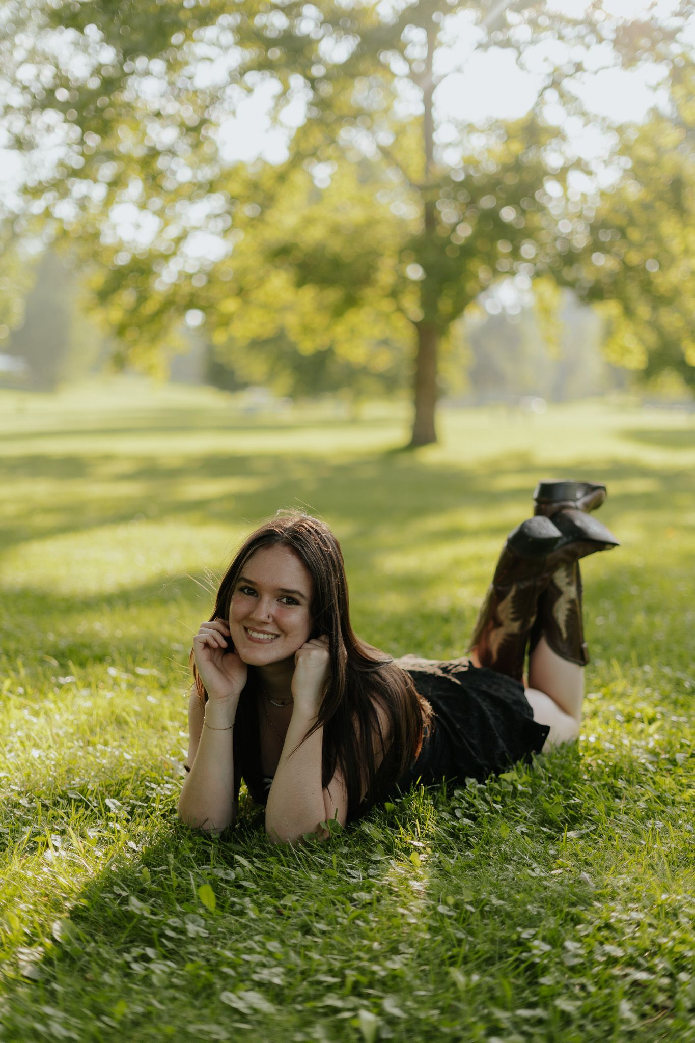 Young woman in black dress lying on green grass in sunny park.