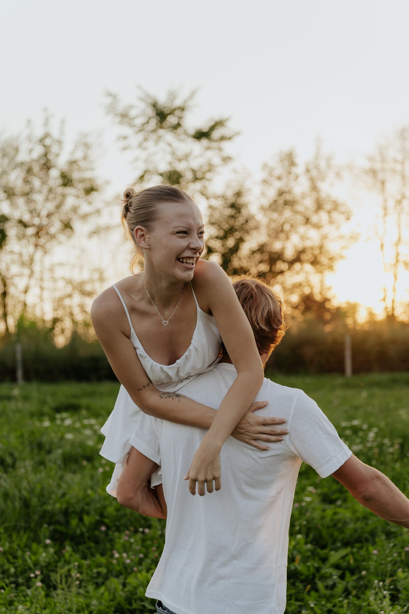 Laughing woman being lifted by her partner in a sunny green field during golden hour.
