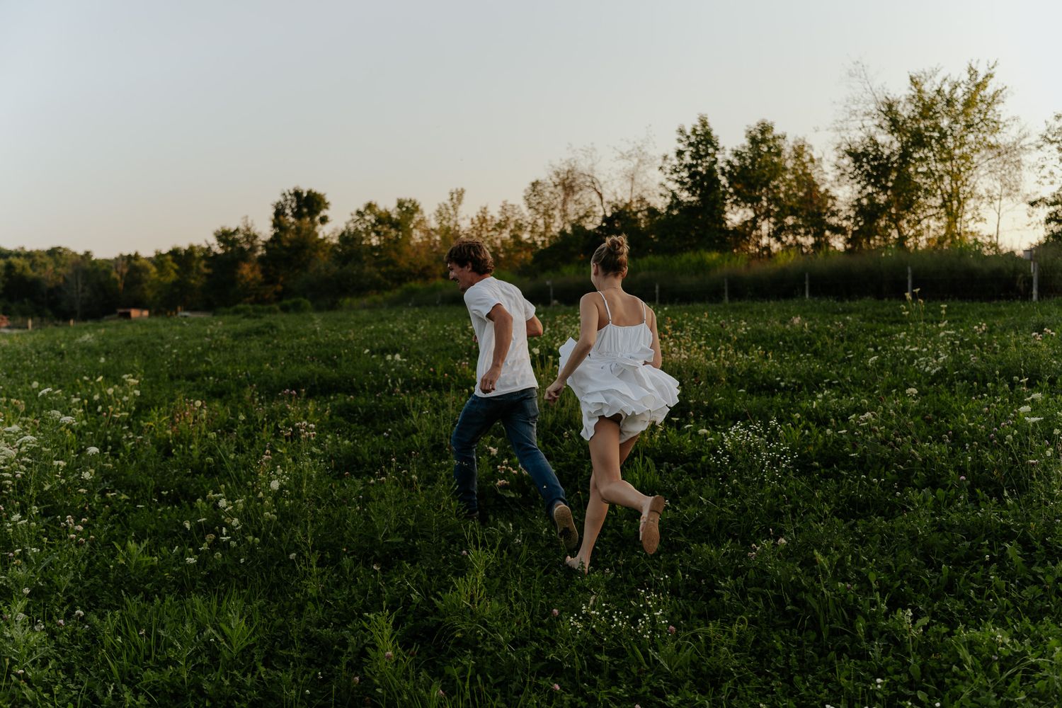 Couple running barefoot through a wildflower meadow at sunset, holding hands in nature.