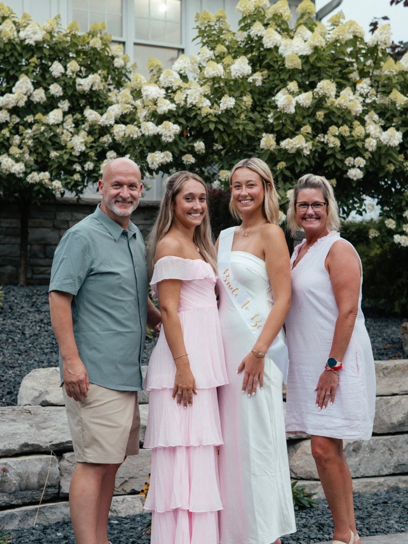 Family of four poses in front of blooming white hydrangeas, dressed in elegant summer attire.