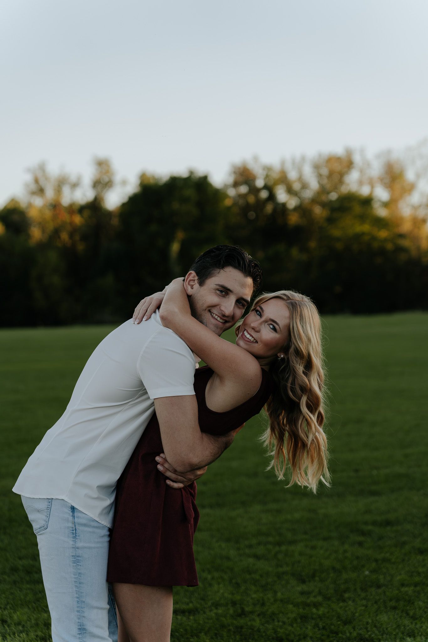 Happy couple hugging and smiling in an open green field during a golden hour photo session.