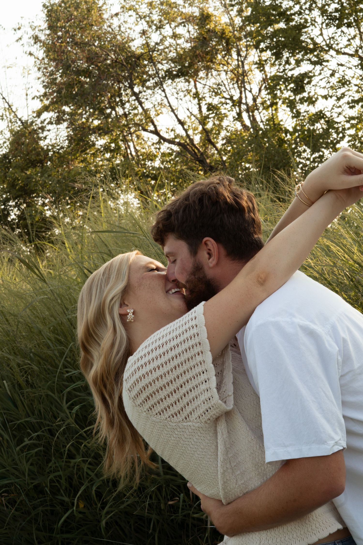 Couple sharing a romantic kiss in a lush green field at golden hour sunset.