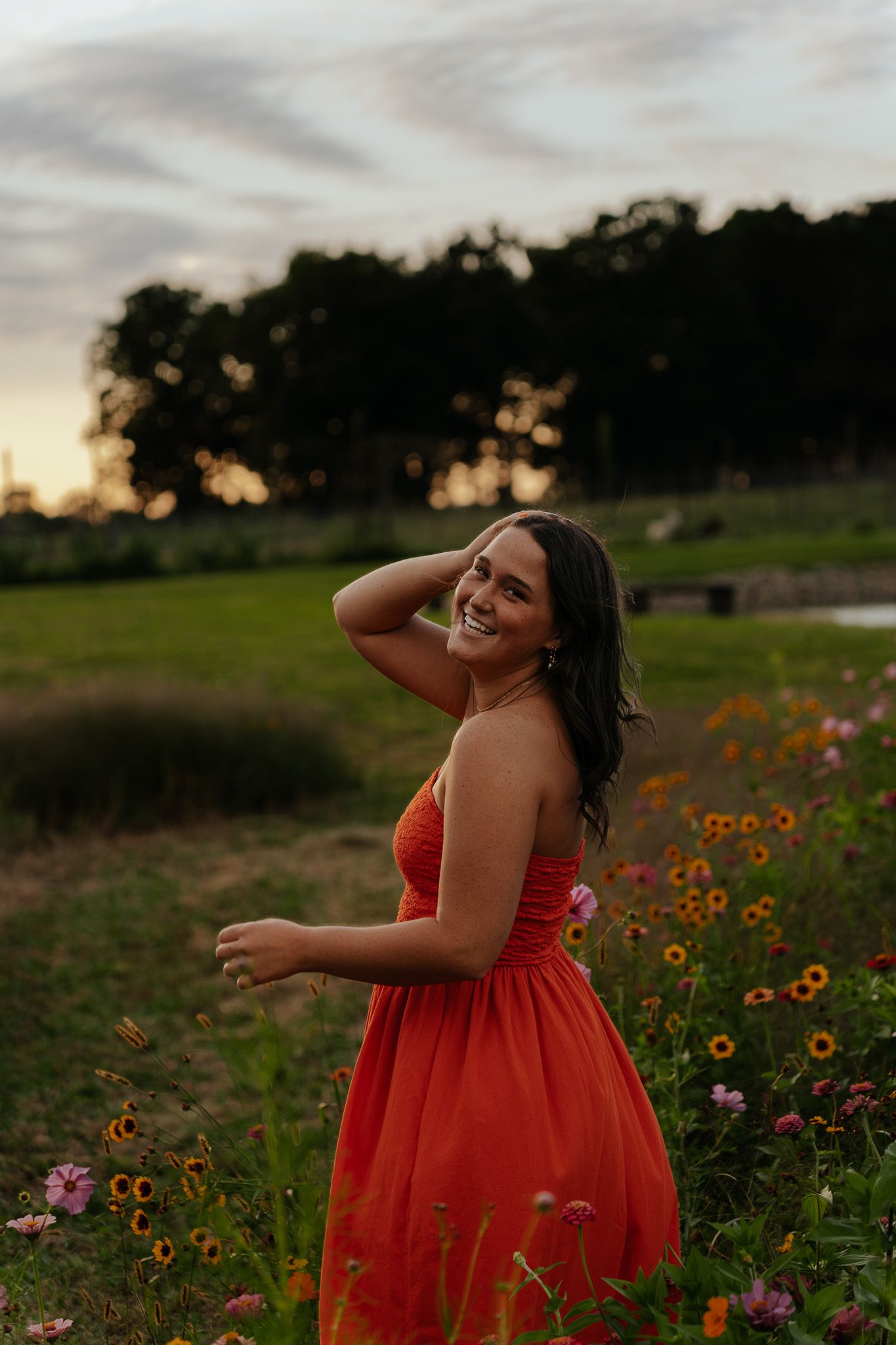 Young woman in red dress smiling in wildflower field at sunset.