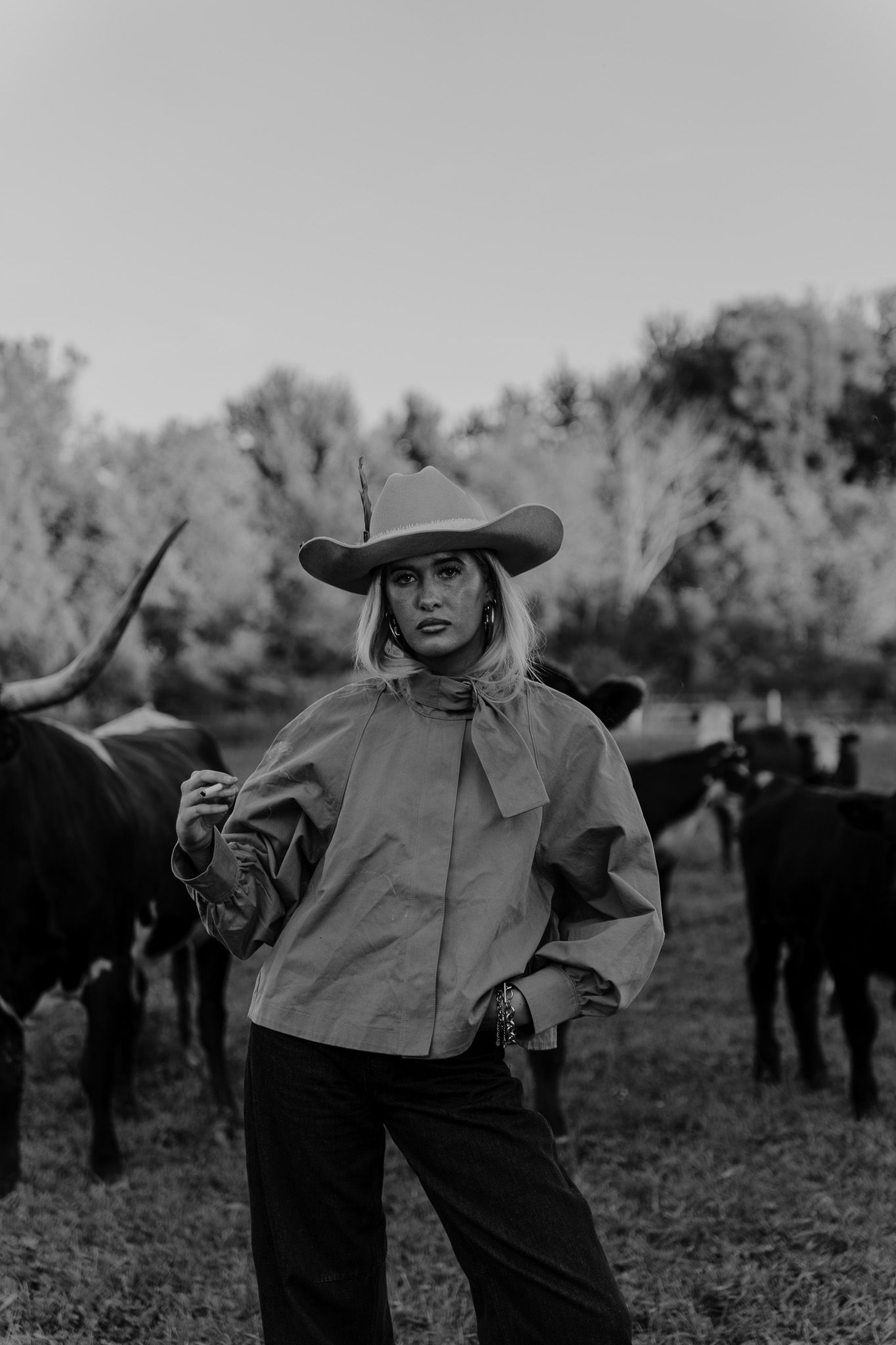 Black and white photo of woman in cowboy hat standing among cattle in a field.