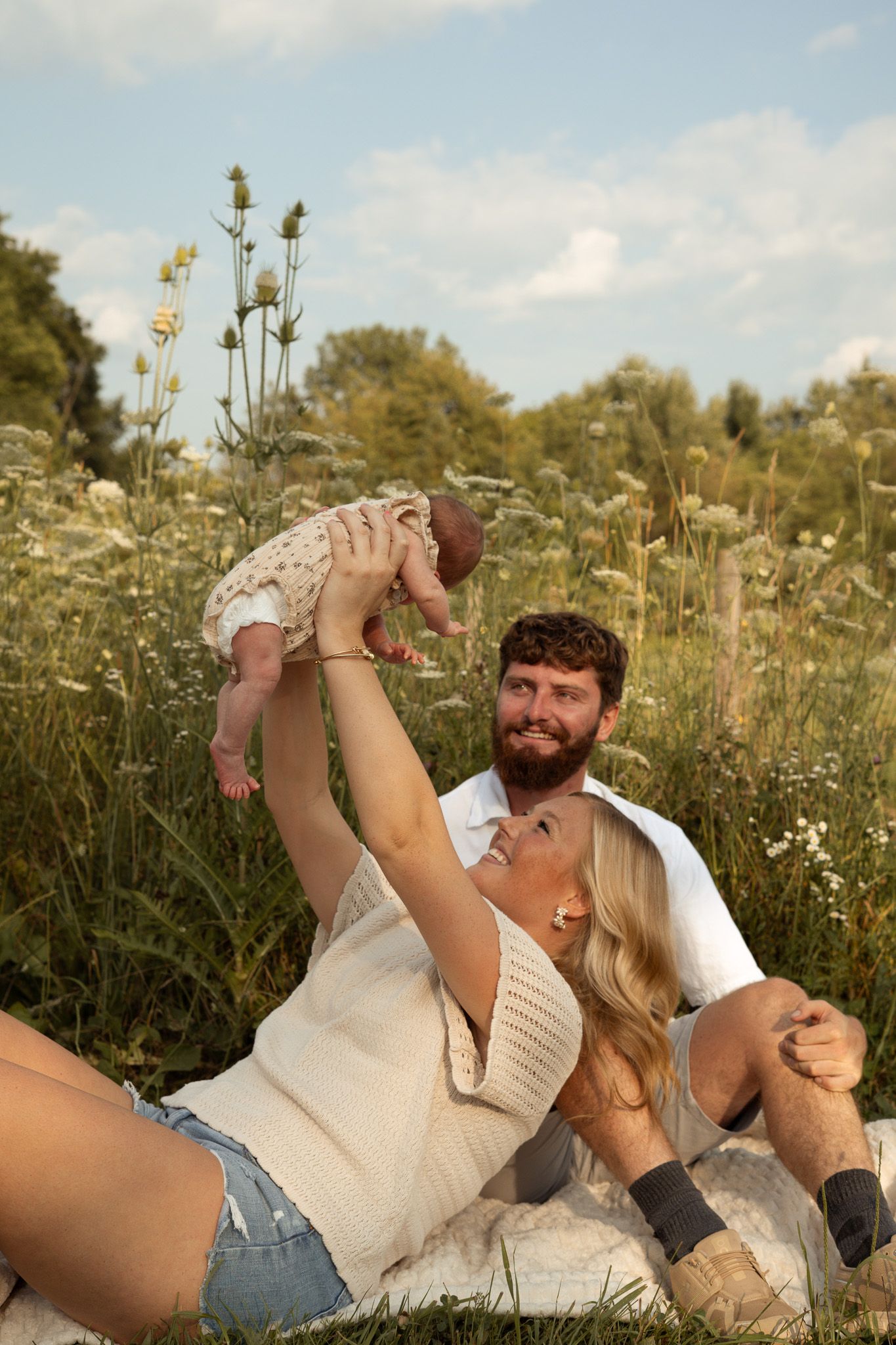 Happy family with newborn baby relaxing in a wildflower meadow on a sunny day.
