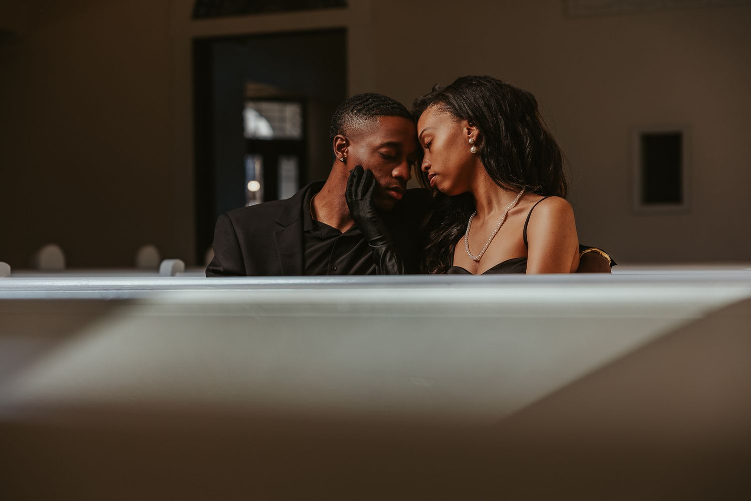 A romantic Black couple shares an intimate moment together, leaning close in a softly lit elegant setting.