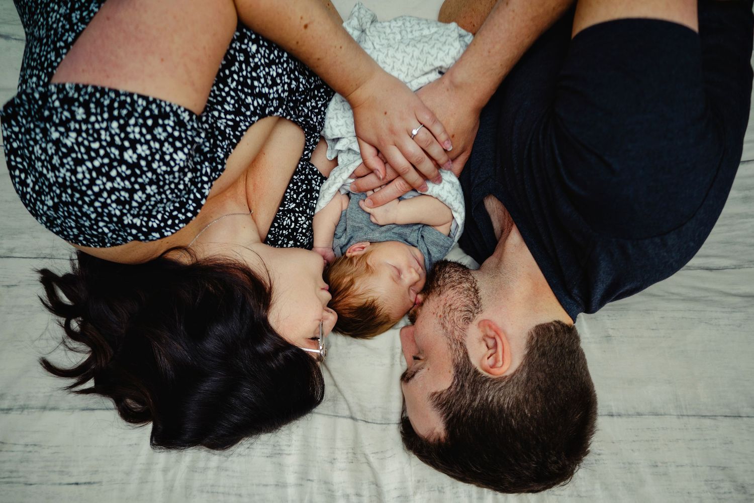 Mom and dad snuggled in bed kissing newborn son. Ottawa Newborn Photography. Ottawa Family Photography