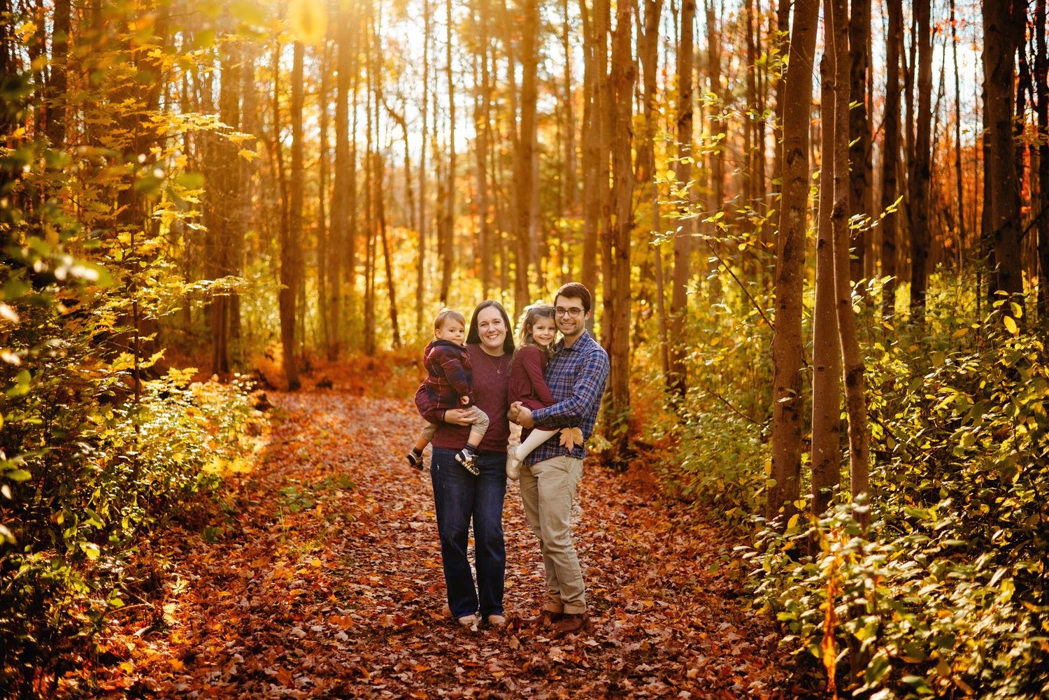 Mom and Dad holding kids in the forest with setting sun. Ottawa Family Photography.