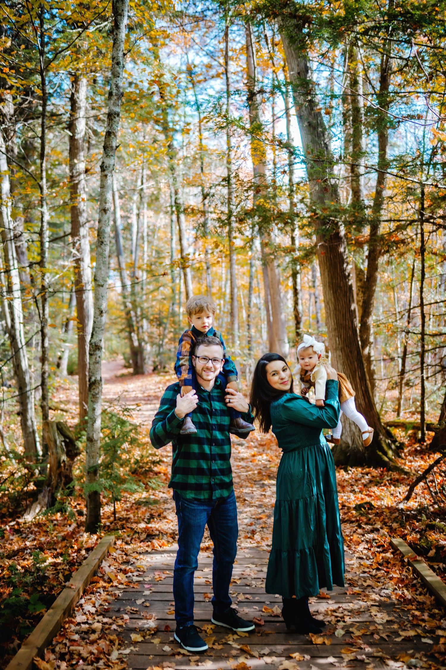 Dad holding son on shoulders while mom holds daughter in the fall leaves. Ottawa Family Photography.