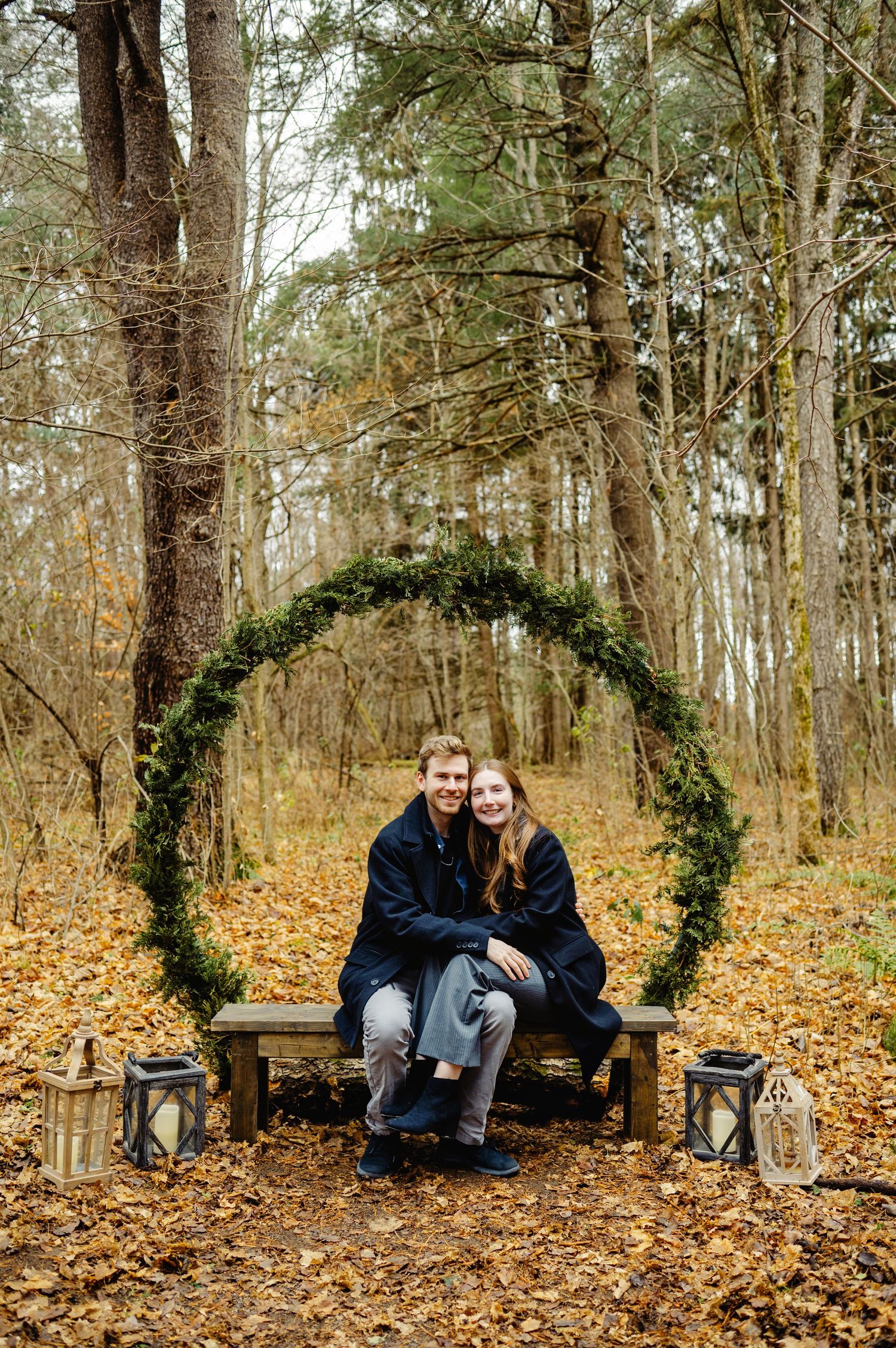 Couple sitting by Christmas greenery arch. Ottawa Christmas Mini's Photographer.