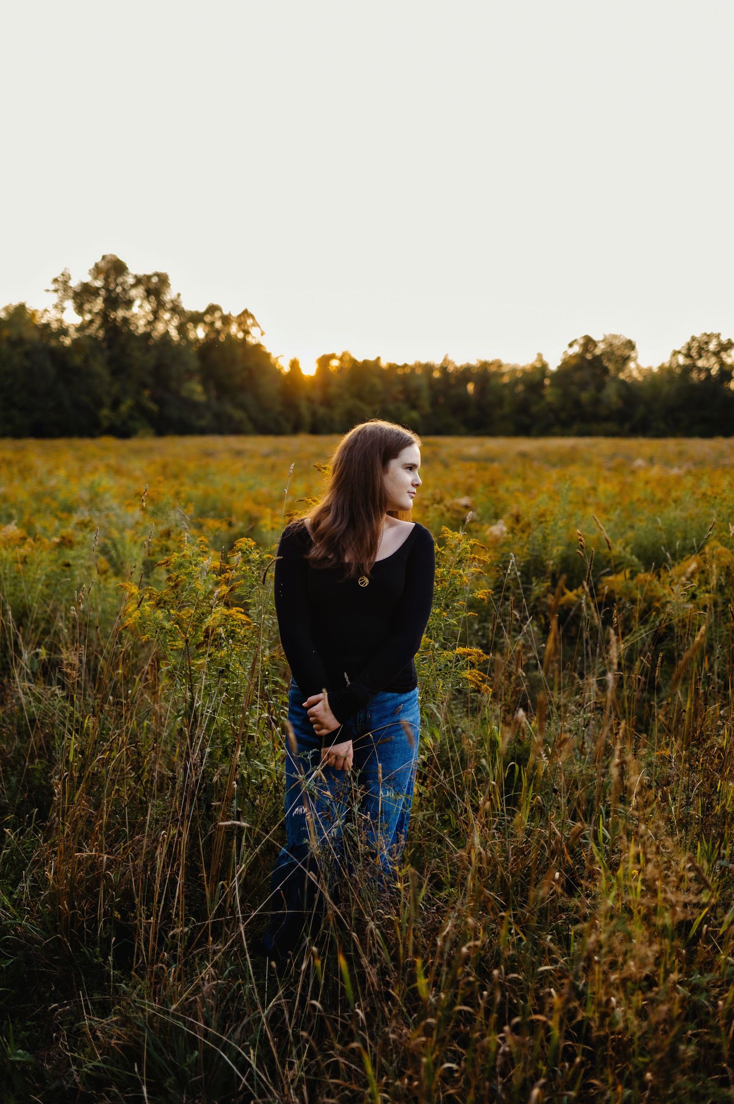 Teen girl standing in the tall grass looking into the distance. Ottawa Family Photography.