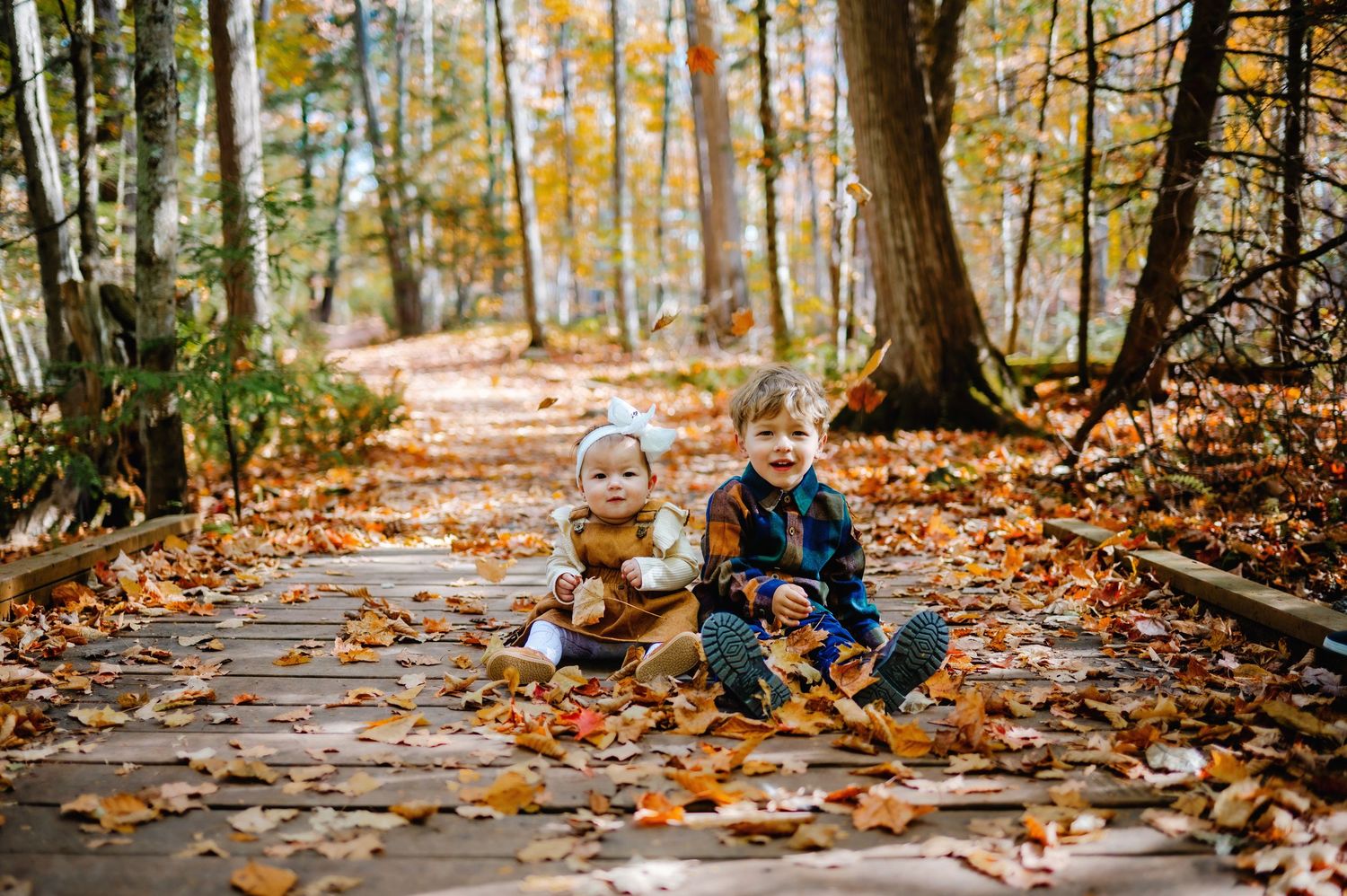 Brother and sister sitting together on bridge with leaves around them. Ottawa Family Photography.