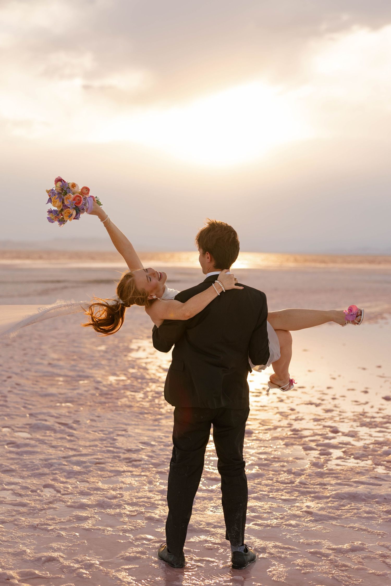 Wedding couple performs romantic dips and poses on reflective pink lake at sunset in Utah