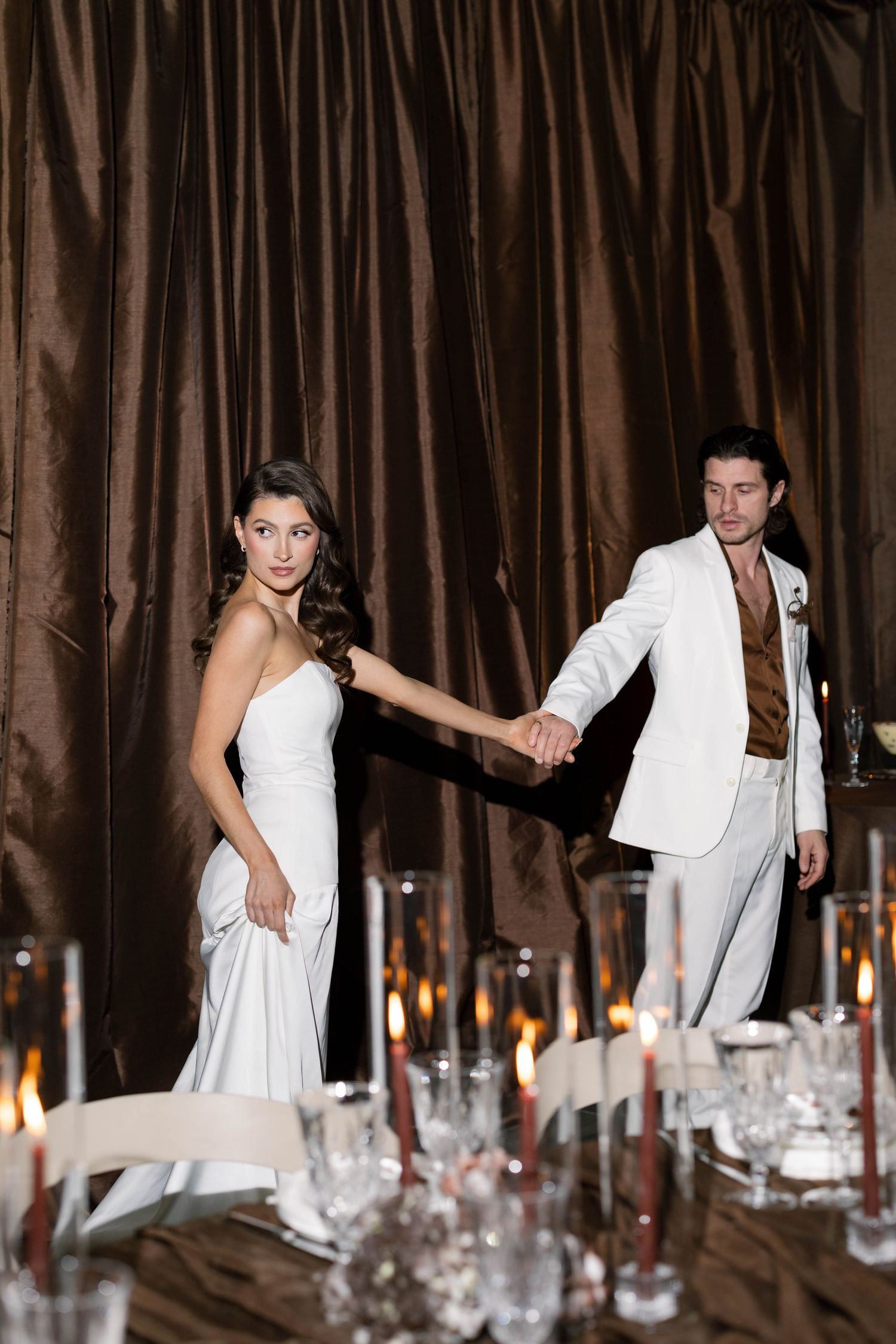 Candlelit dinner table setting with couple in white formal attire.