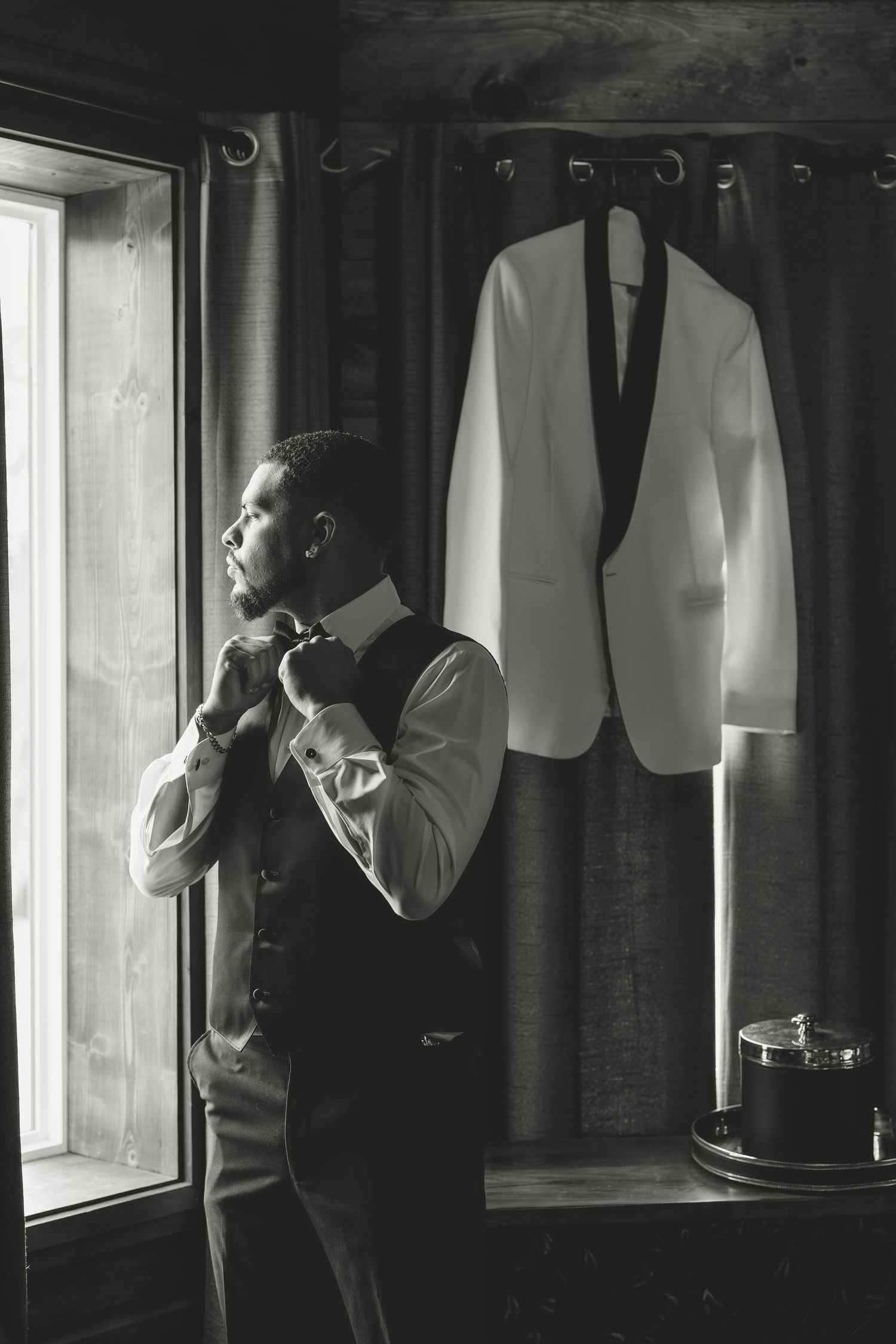 Black and white photo showing a formal suit preparation with a white dinner jacket hanging while adjusting attire.