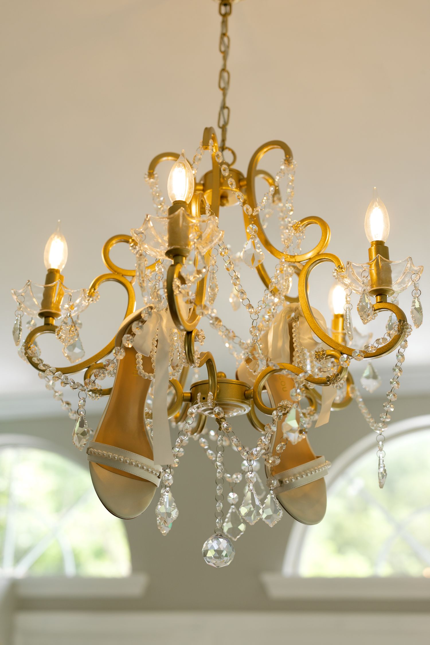 Elegant gold crystal chandelier with candle lights and cascading crystal drops hanging from white ceiling.