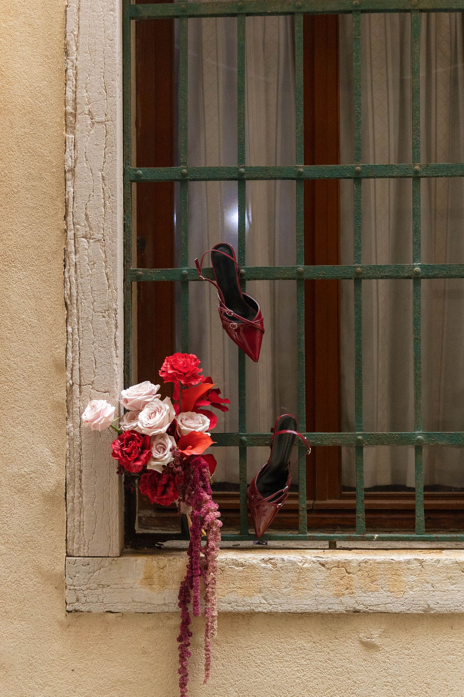 Red and pink floral arrangement displayed in a rustic window frame.