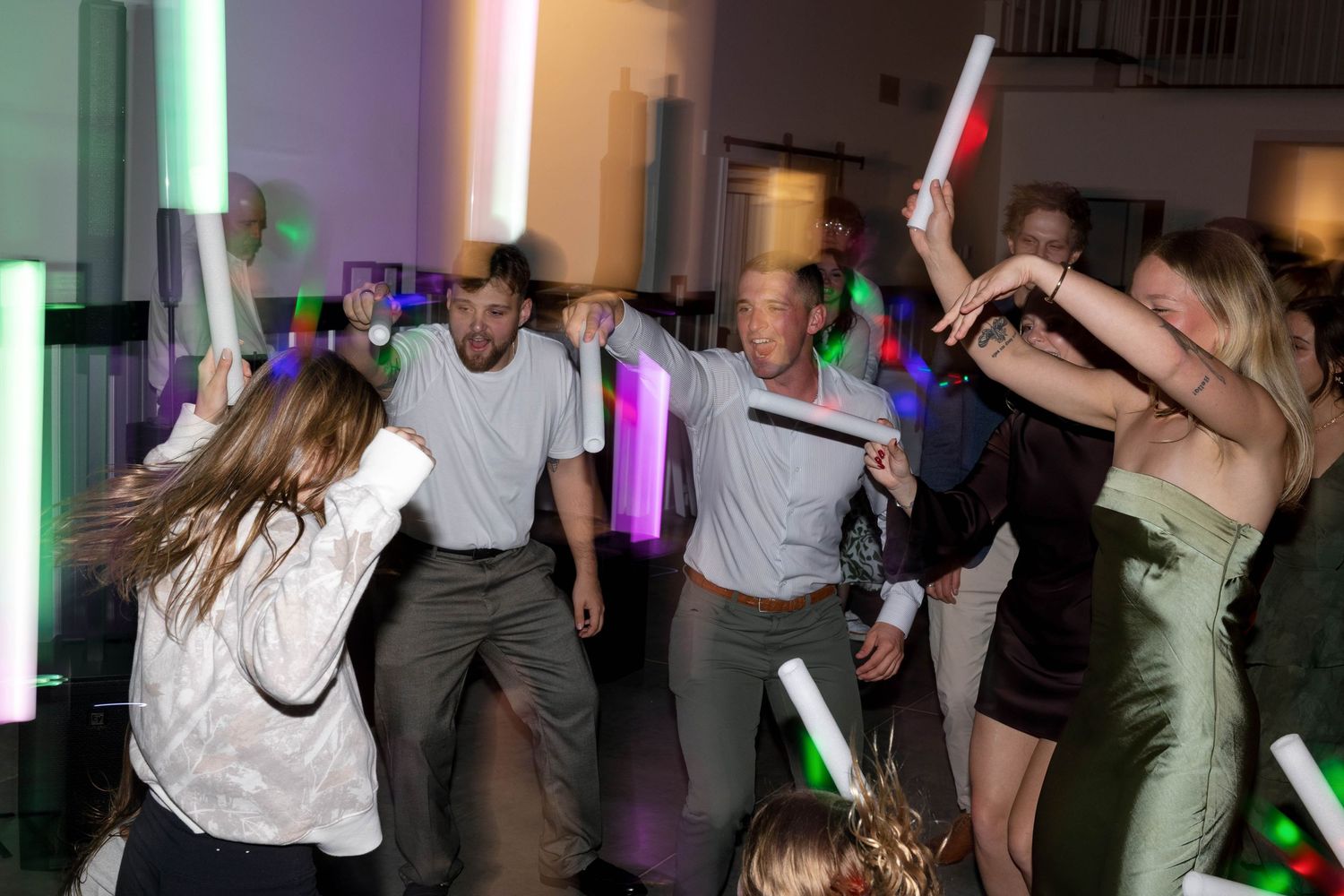 Wedding guests dancing with colorful light-up wands on the dance floor.