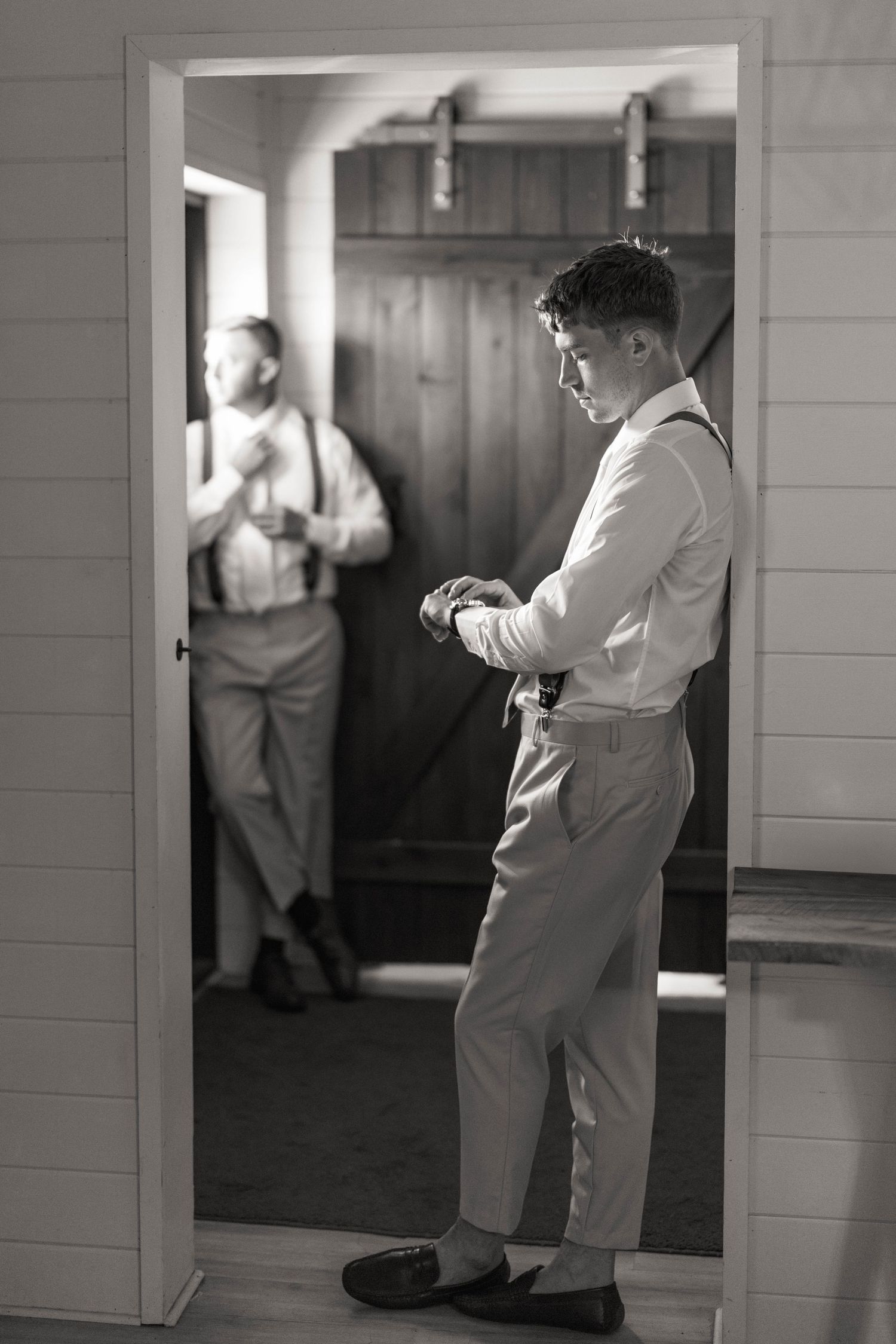black and white image of a groom in a door frame with groomsman in the background