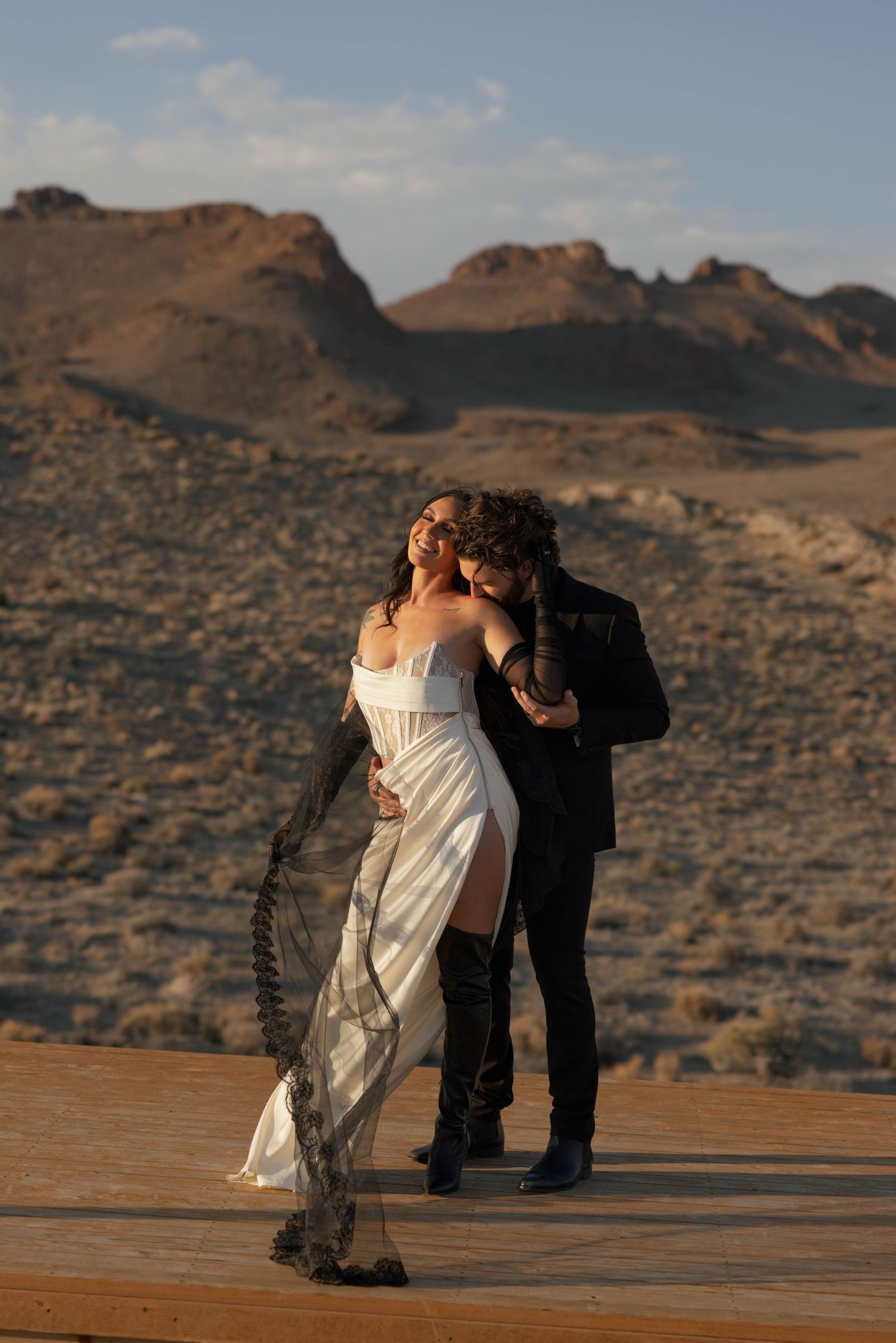A romantic couple dips and dances against a desert mountain backdrop during sunset.