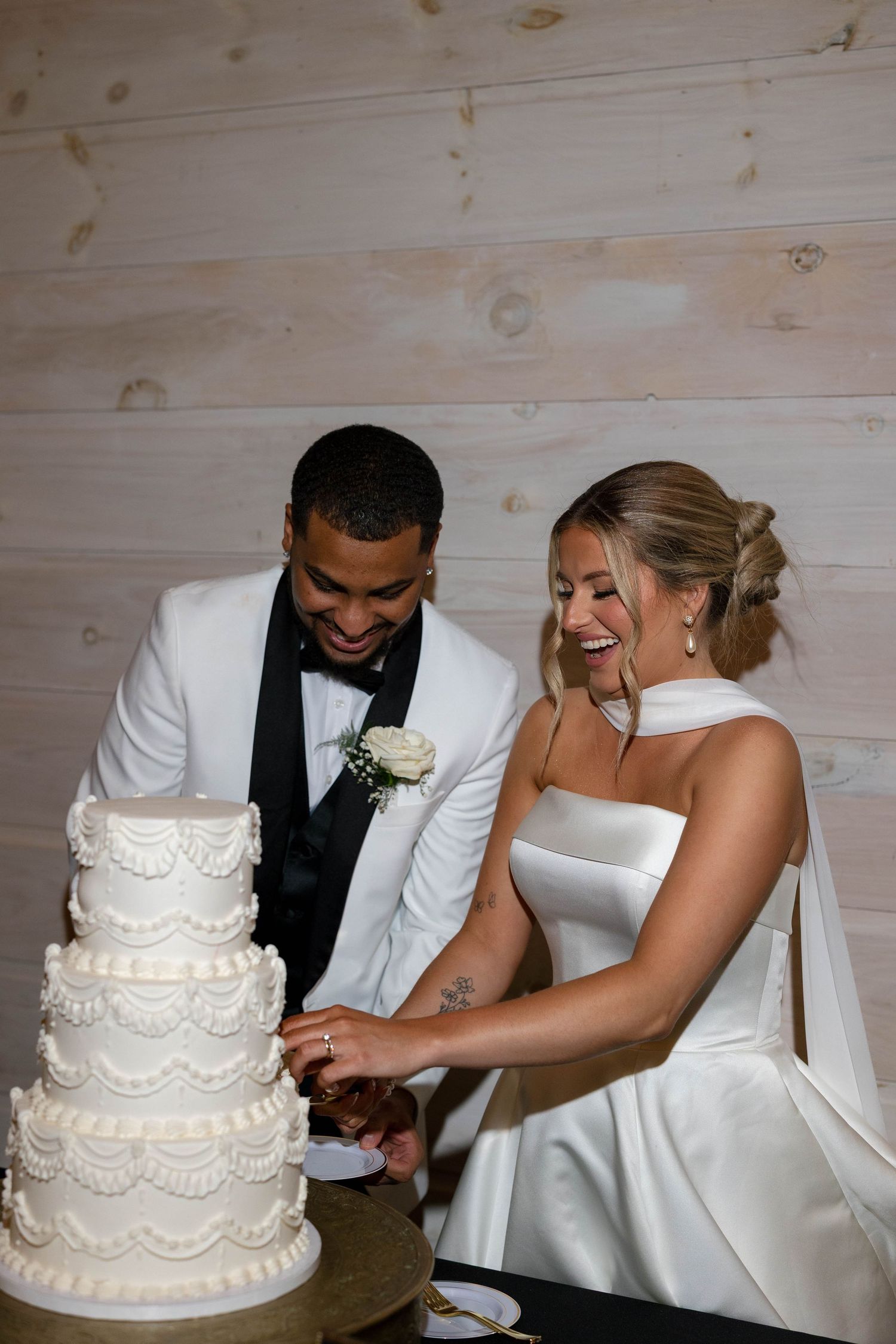 A couple cutting their traditional white tiered wedding cake together.