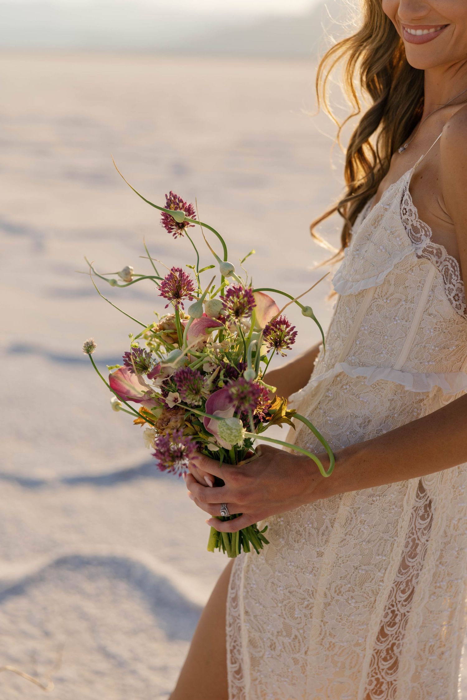 Elegant bridal bouquet with pink and purple wildflowers against a sunlit background.