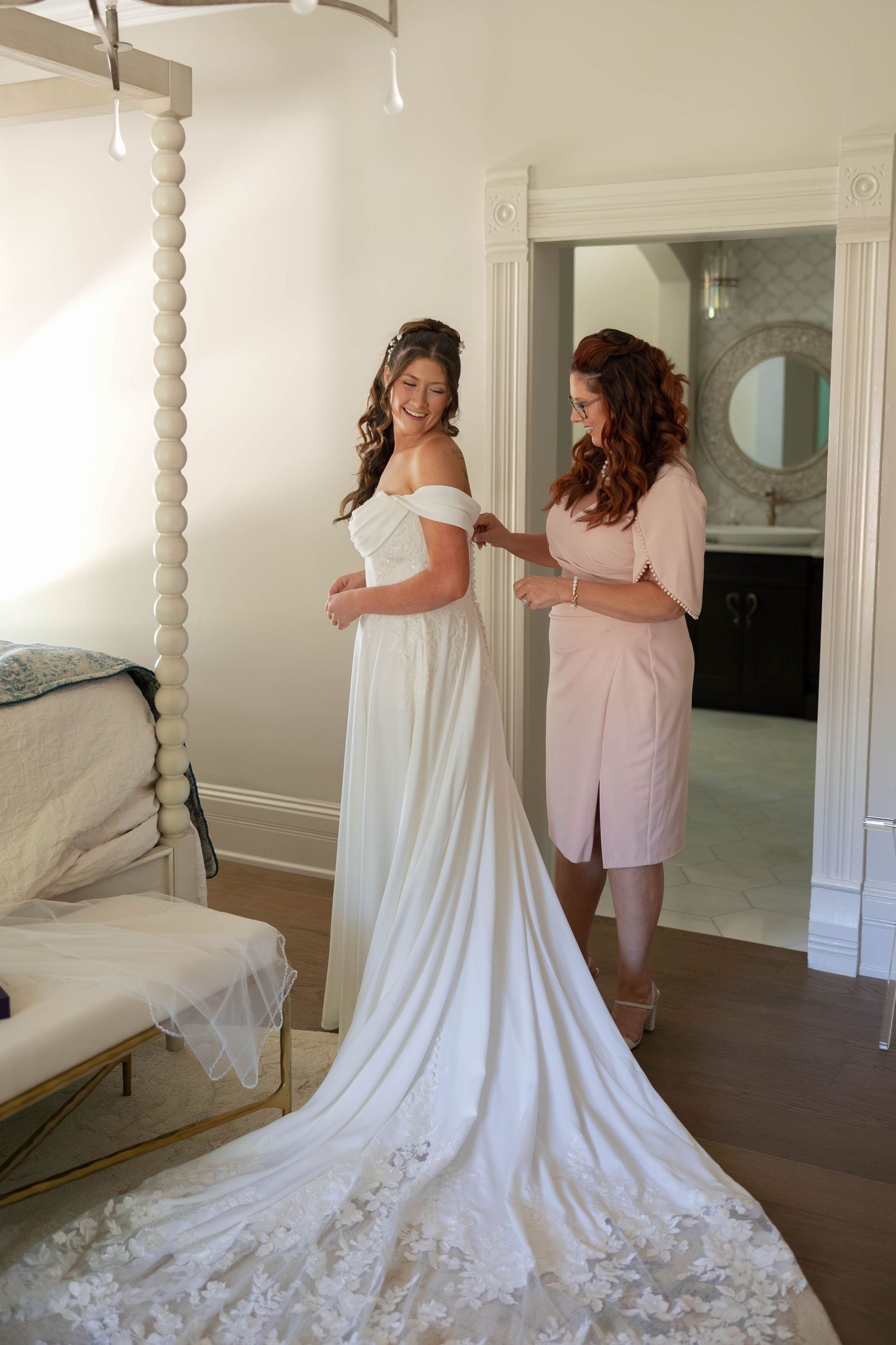 Elegant white wedding dress with long train being fitted in a bright room.