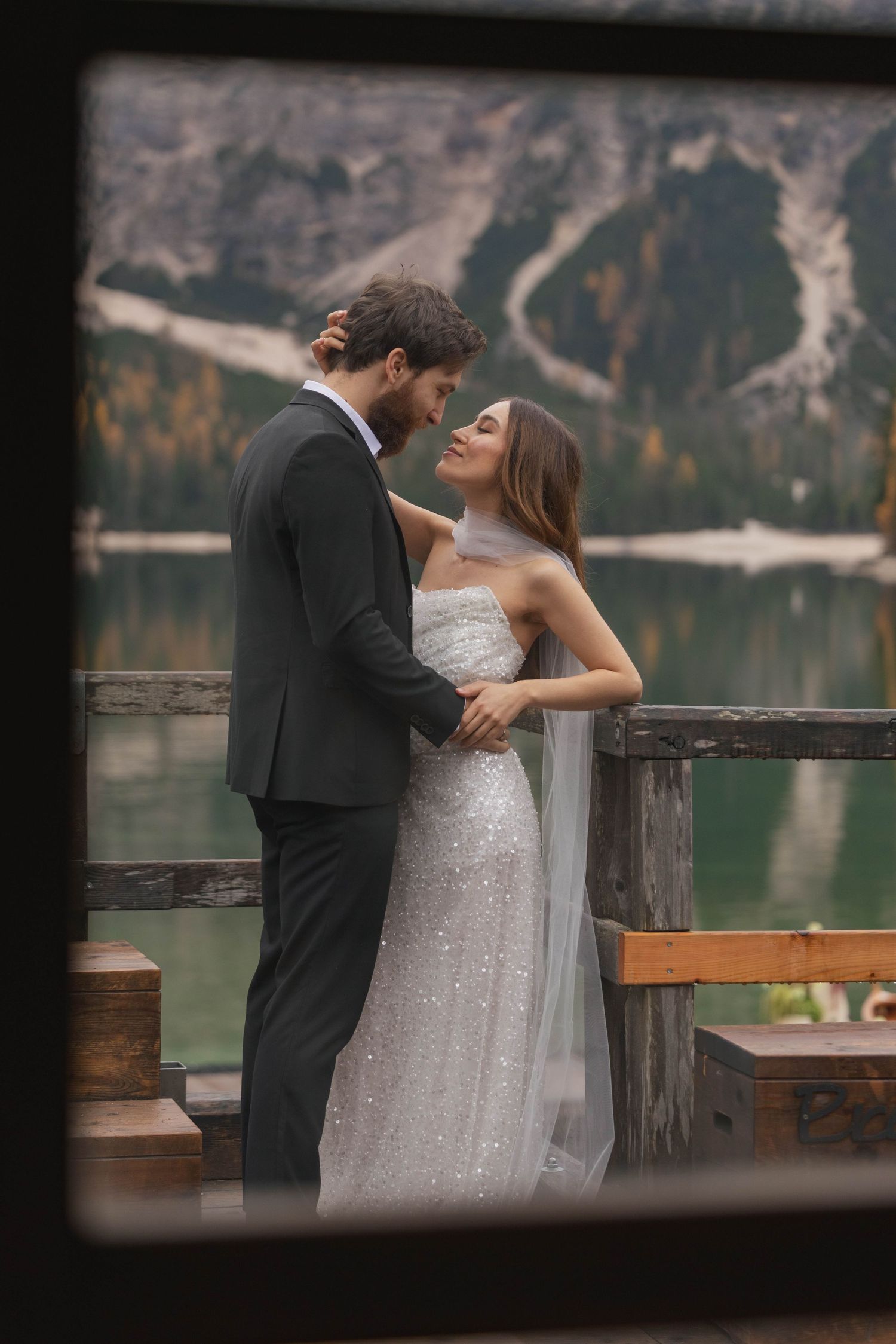 Romantic couple embracing on a dock with mountain lake backdrop at Lago di braies