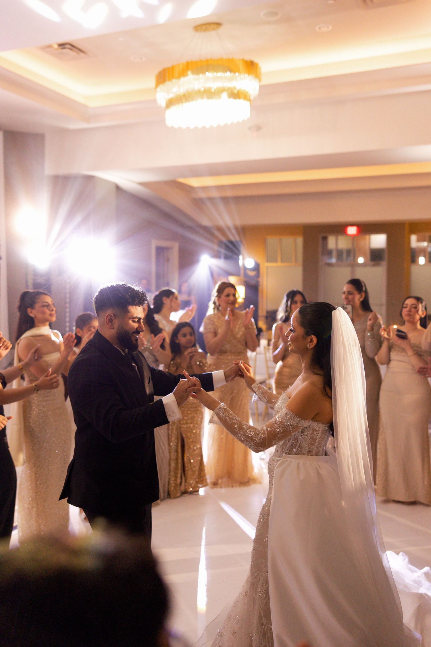 Wedding guests dancing and celebrating in an elegant ballroom with crystal chandeliers.