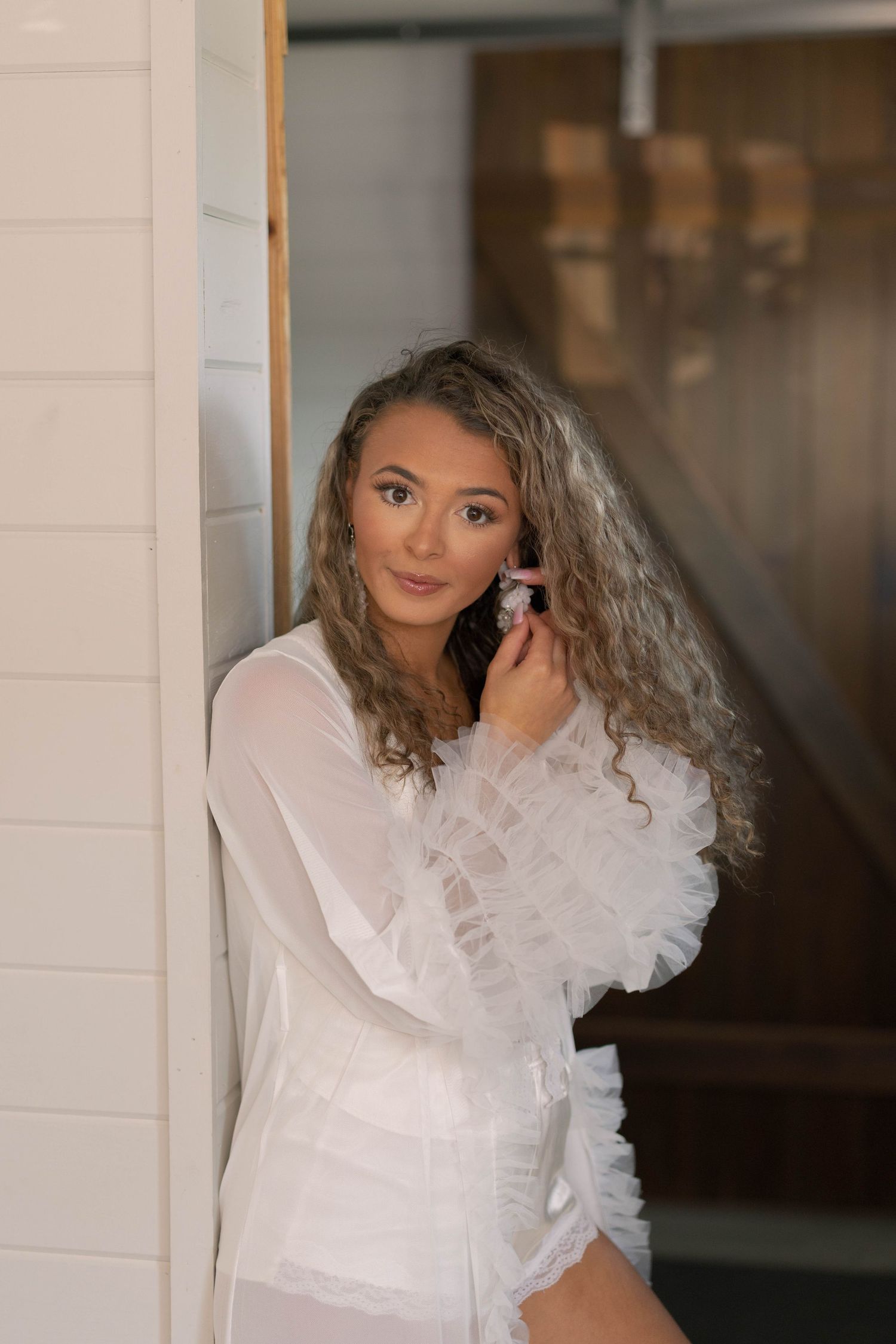Bridal boudoir photo featuring white lace robe in soft natural lighting.