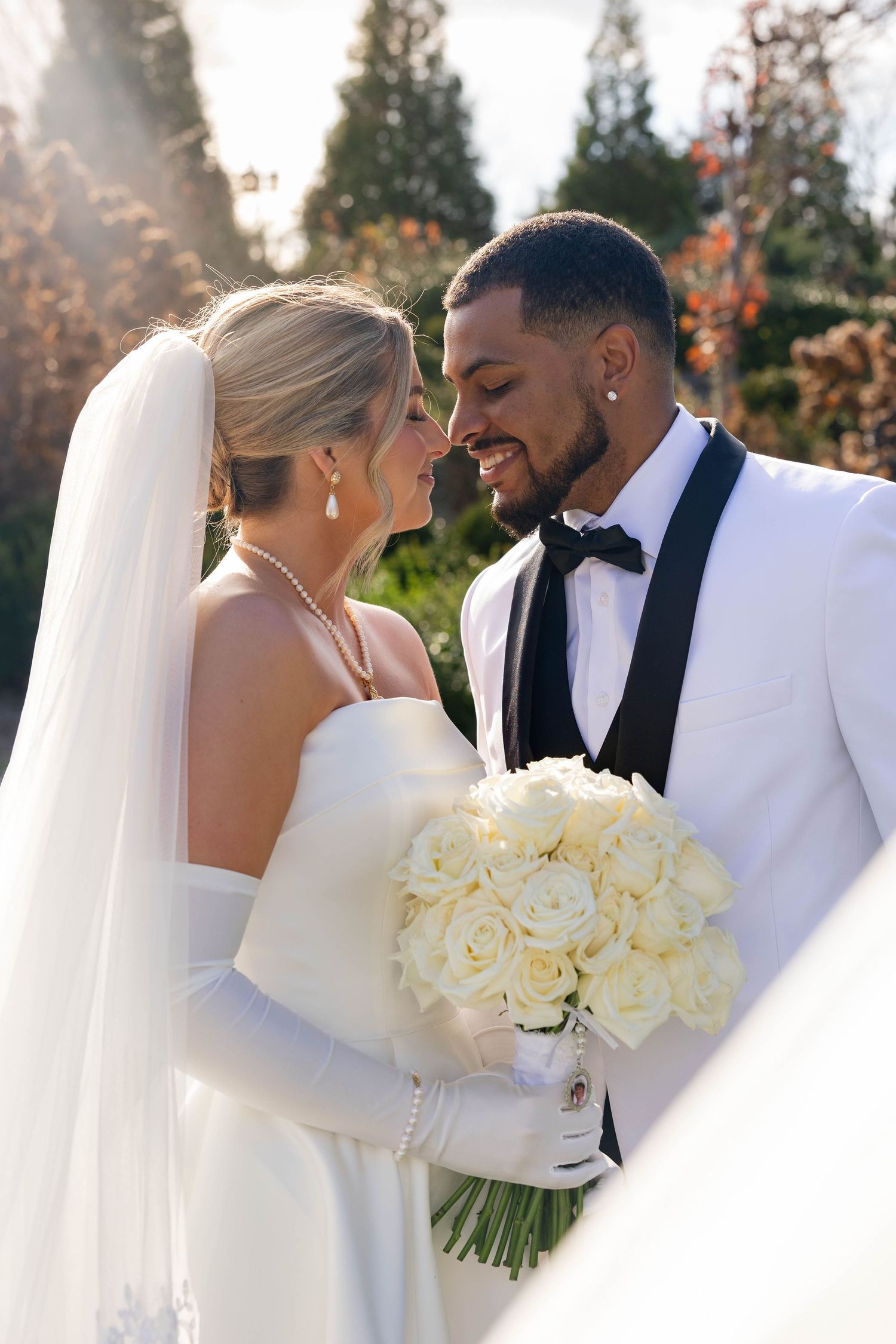 Elegant wedding couple poses with white rose bouquet in winter garden setting.