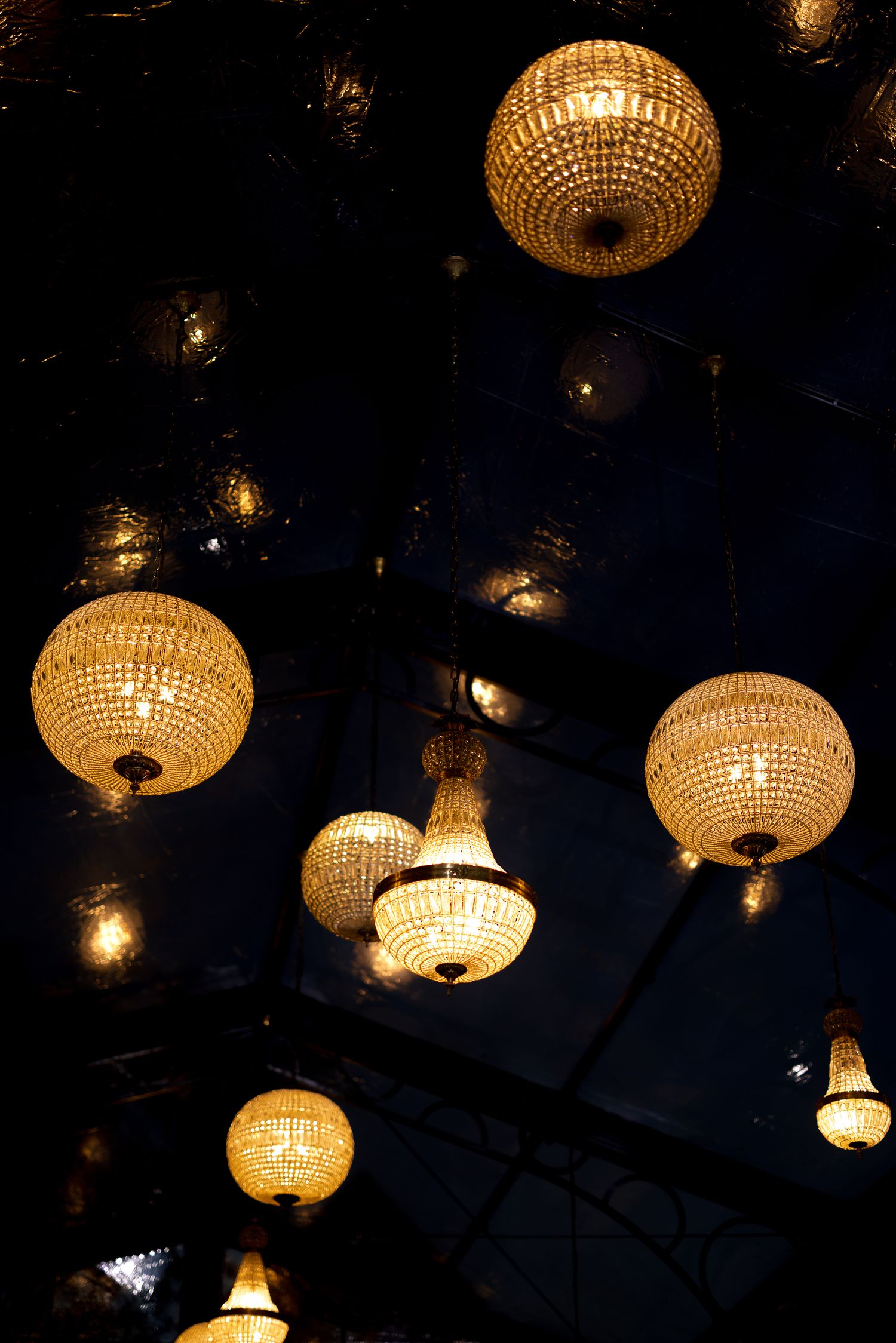 Elegant crystal ball chandeliers glowing warmly against a dark ceiling in a luxurious interior setting.